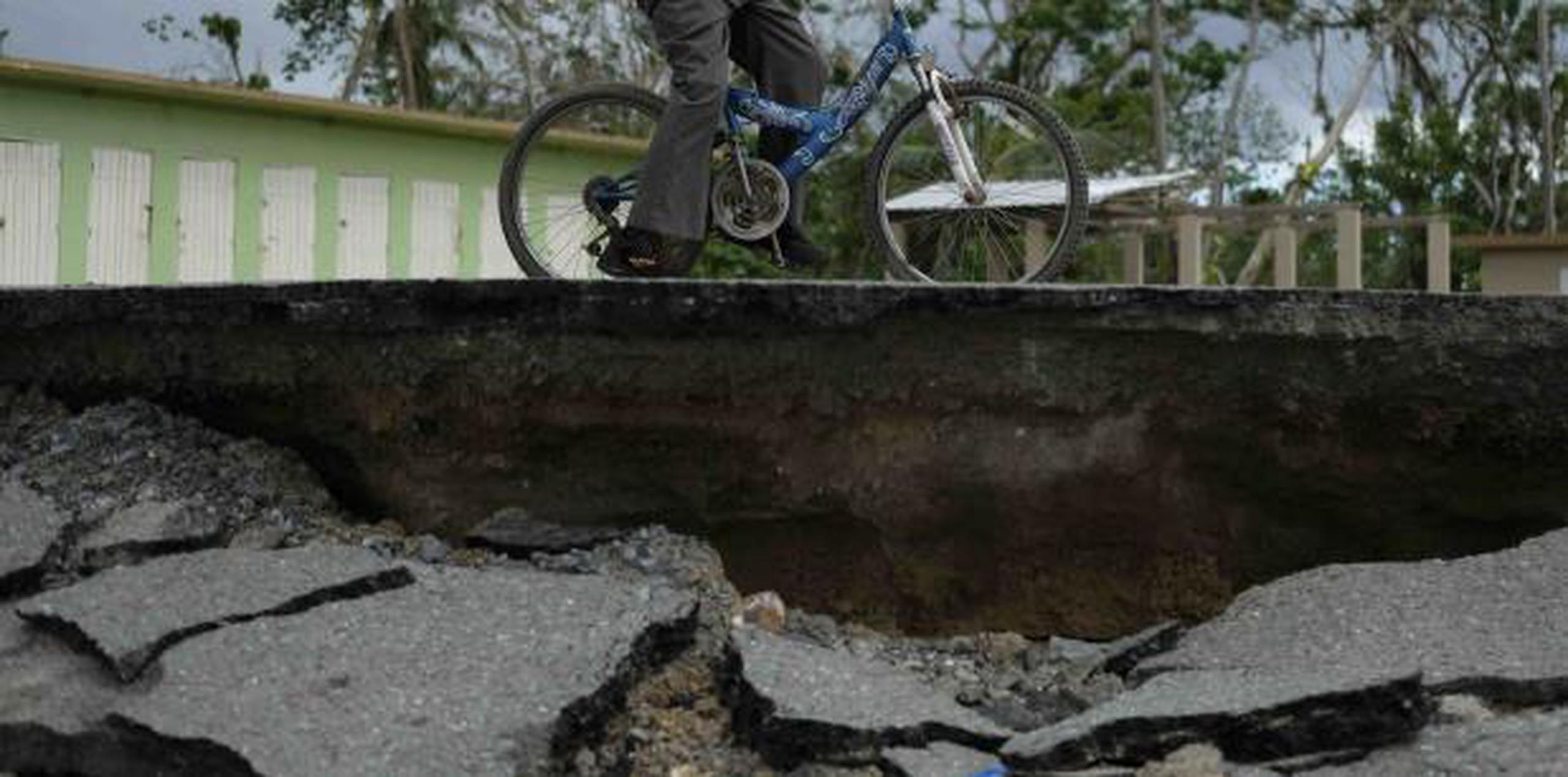 Un ciudadano corre bicicleta al lado de una carretera destruida en Añasco. (archivo)