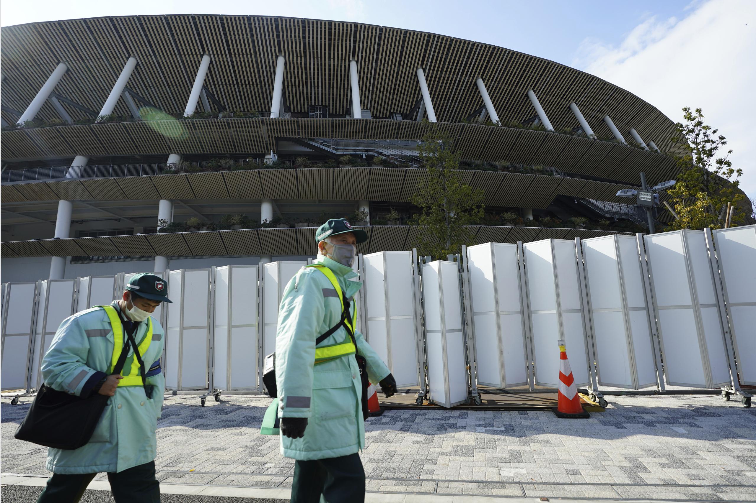 Inspectores de estacionamiento con máscaras faciales para protegerse contra la propagación del coronavirus pasan por el Estadio Nacional de Japón, donde se planea la ceremonia de apertura y muchos otros eventos para los Juegos Olímpicos de Tokio 2020.