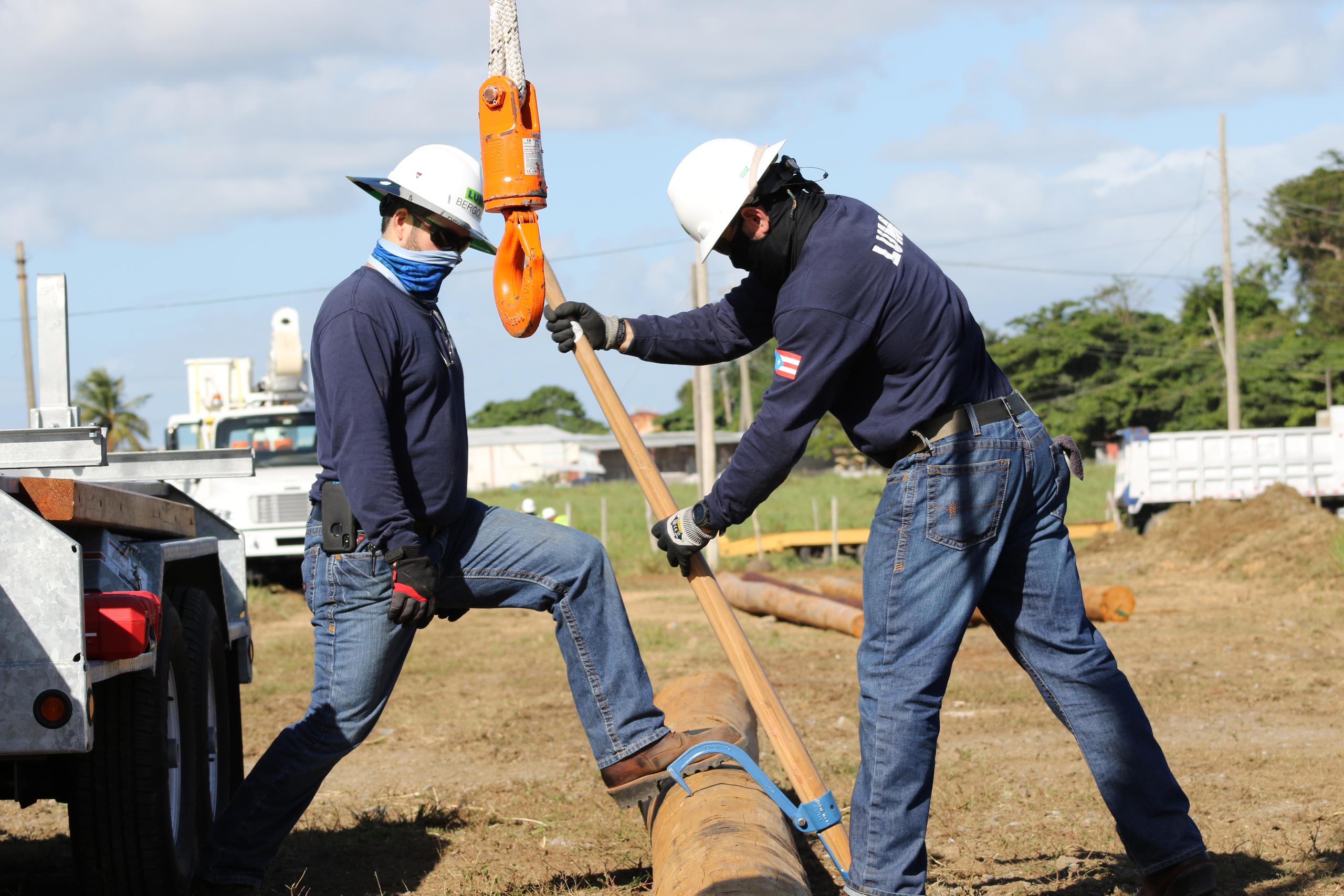 Dos graduados del Colegio de Entrenamiento Técnico de LUMA en Canóvanas se preparan para levantar un poste de electricidad.