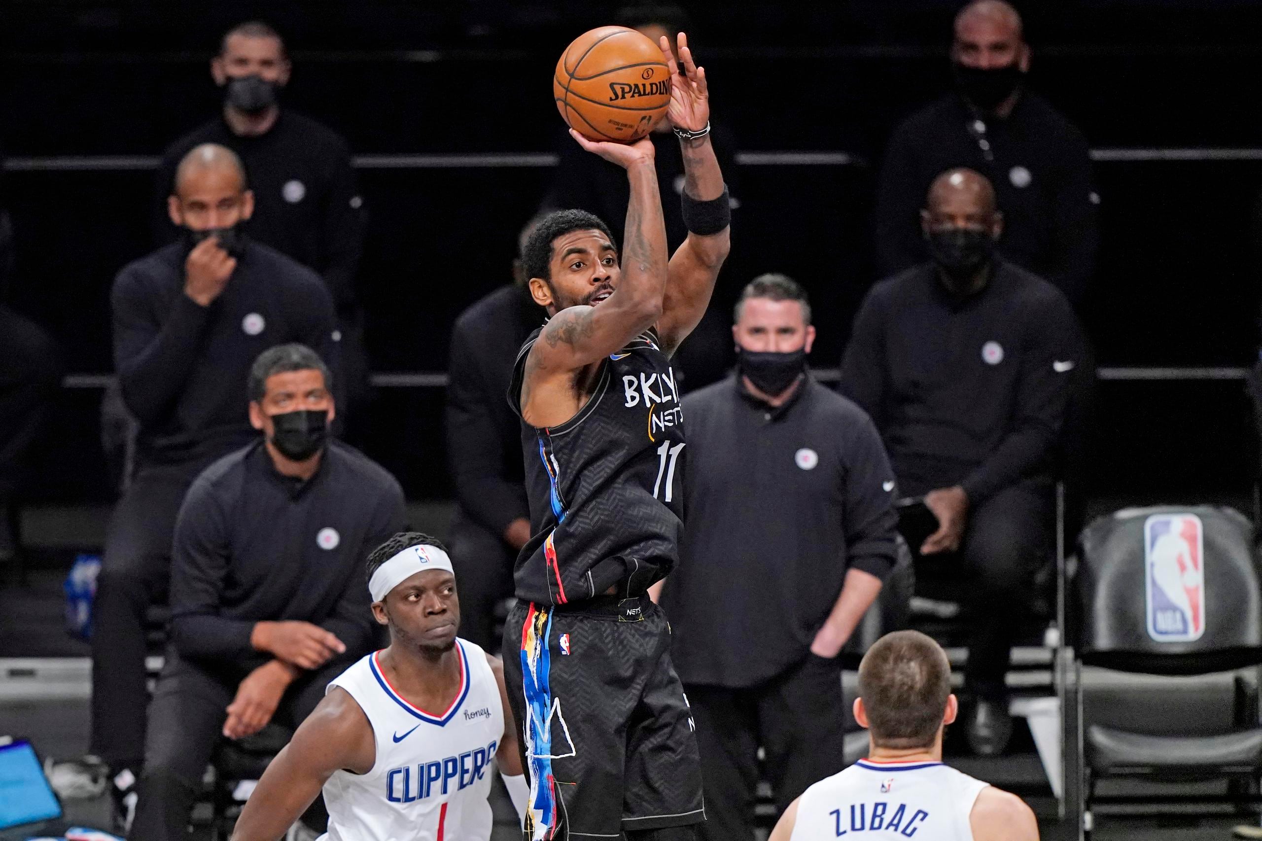 El base de los Nets de Brooklyn Kyrie Irving lanza el balón mientras observan Reggie Jackson e Ivica Zubac de los Clippers de Los Ángeles.