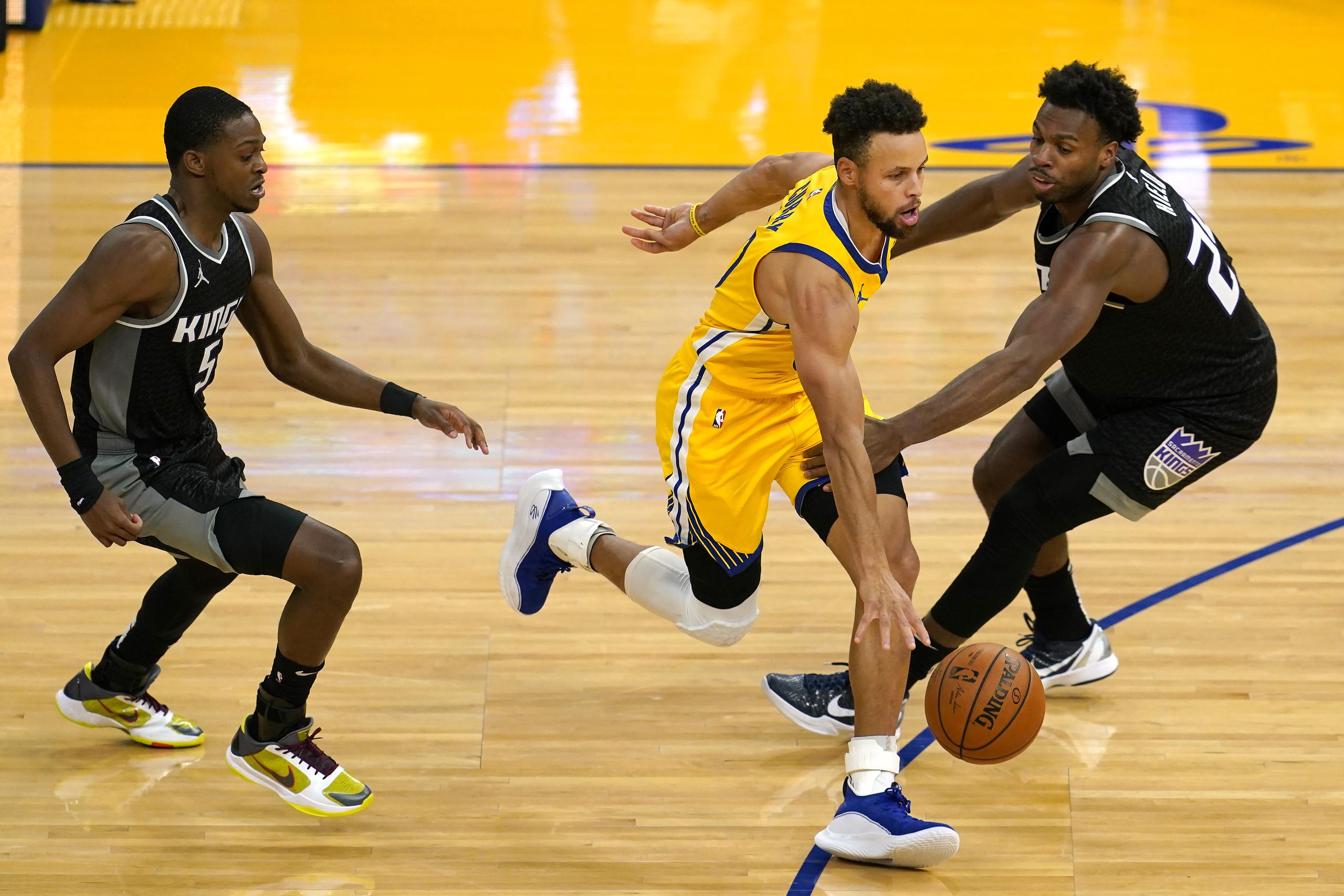 Stephen Curry, de los Warriors de Golden State, pasa dribleando el balón entre De'Aaron Fox (5) y Buddy Hield durante la segunda mitad del partido ante los Kings de Sacramento.