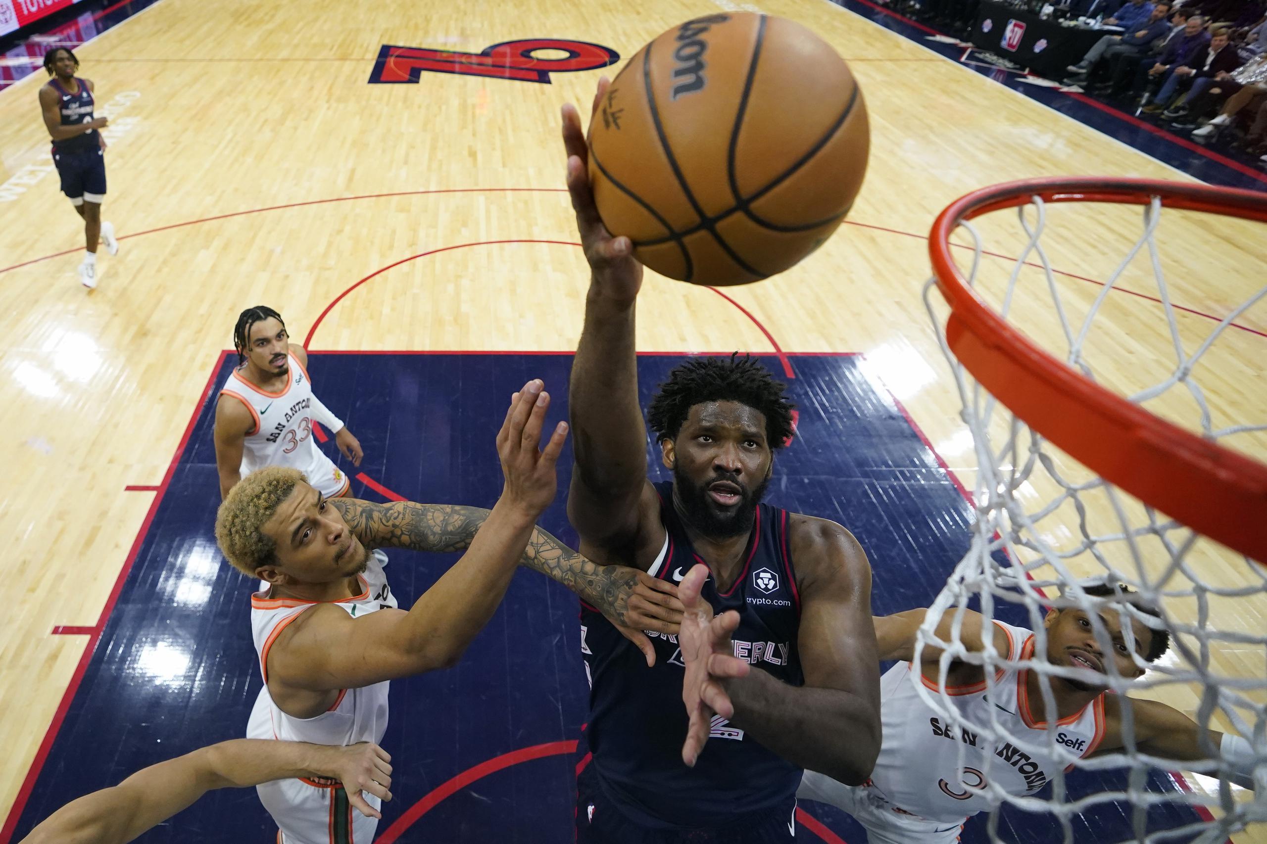 Joel Embiid, centro, de los 76ers de Filadelfia, toma un disparo entre Jeremy Sochan, izquierda, y Keldon Johnson, de los Spurs de San Antonio, durante la segunda mitad del juego de baloncesto de la NBA, el lunes 22 de enero de 2024, en Filadelfia.