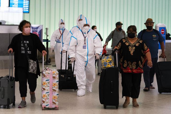 Miembros de la tripulación de Air China caminan vestidos con trajes de materiales peligrosos por el área de llegadas del Aeropuerto Internacional de Los Ángeles el 30 de noviembre de 2021.