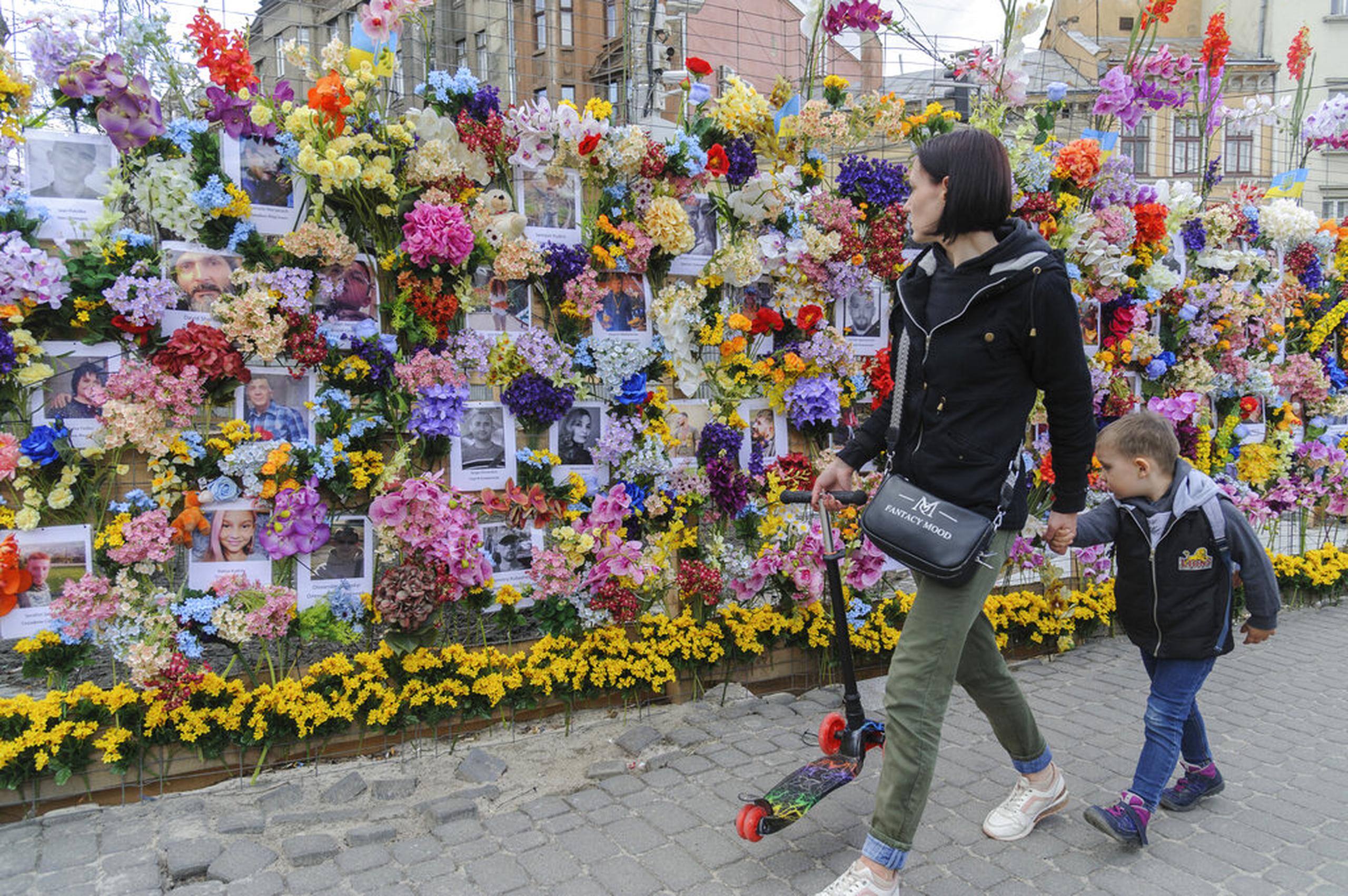 Transeúntes contemplan un muro de flores artificiales instalado por la Fundación Wall of Flowers, con sede en Estados Unidos, en memoria de las víctimas de la invasión rusa, en la ciudad occidental de Lviv, Ucrania, el 25 de abril de 2022.