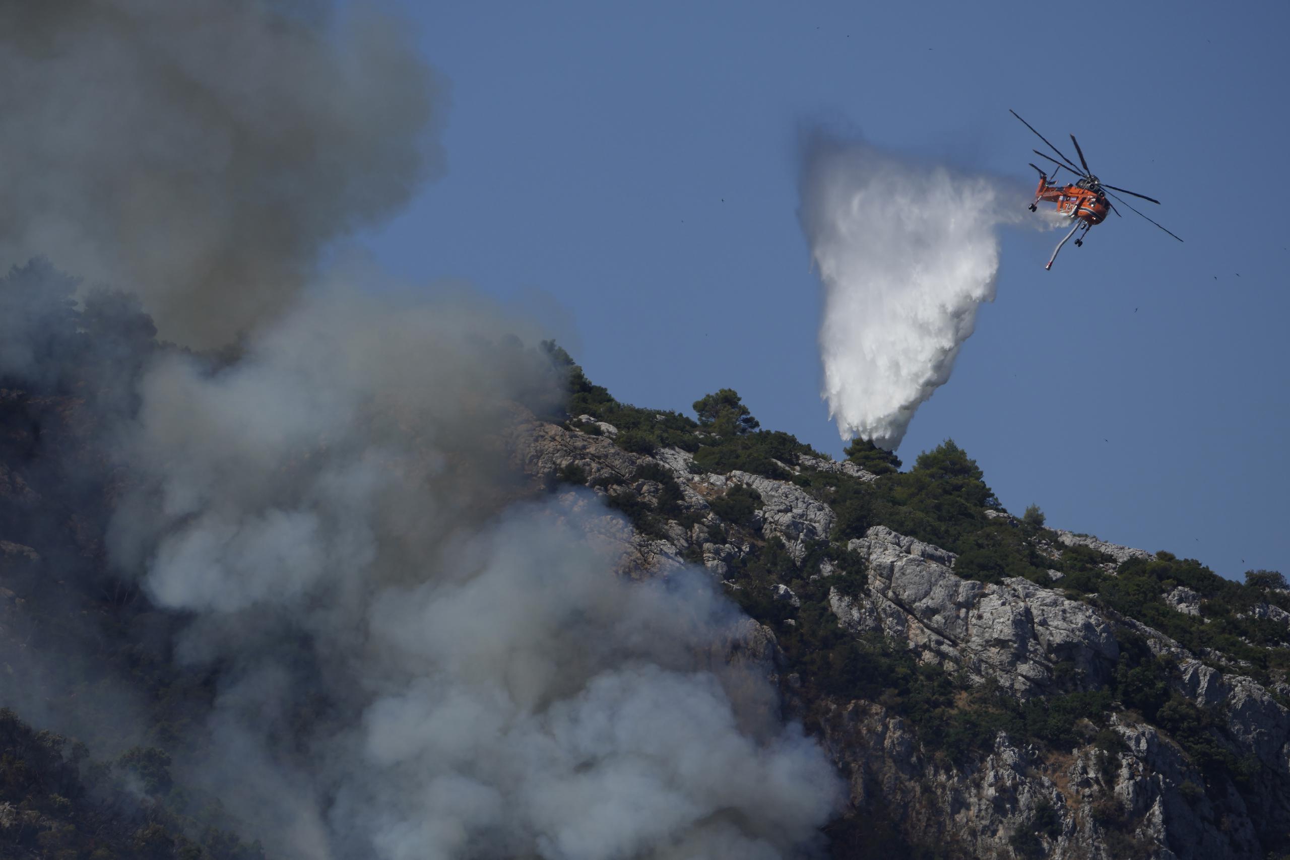 Un helicóptero dejaba caer ague esta mañana sobre el incendio cercano a Malakasa, al norte de Atenas, región en la que se vivió una frenética evacuación el viernes.