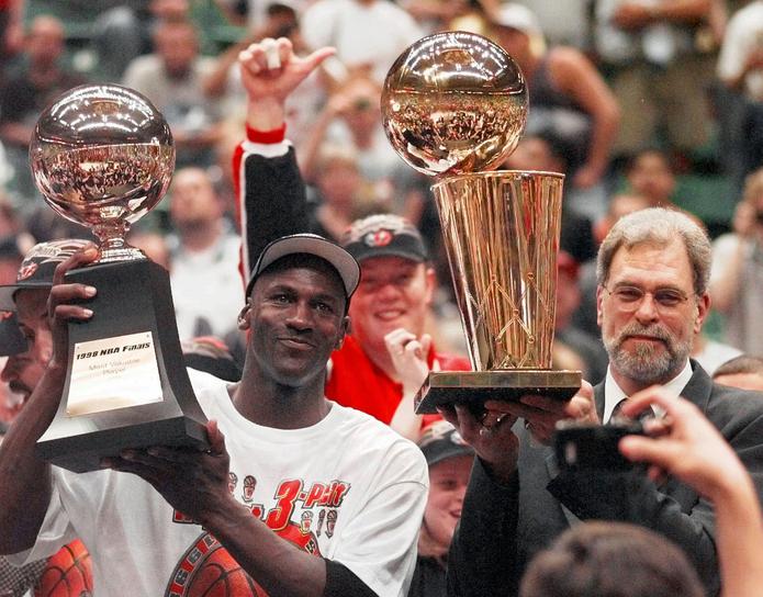 Michael Jordan sostiene el trofeo de Jugador Más Valioso de la serie final de 1998, mientras el dirigente Phil Jackson carga el trofeo de campeones, el sexto para el dúo en ocho temporadas.