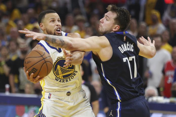 El armador de los Warriors de Golden State, Stephen Curry, a la izquierda, logra escurrir su brazo con el balón por debajo de la defensa de Luka Doncic, de los Mavericks de Dallas, durante el desafío del viernes en San Francisco.
