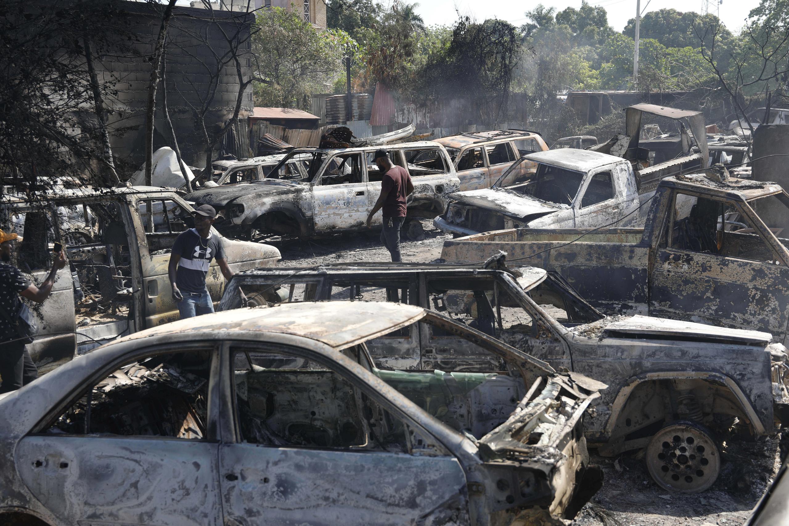 Varias personas buscan piezas rescatables de coches quemados en un taller mecánico incendiado durante la violencia desatada por pandillas armadas en Puerto Príncipe, Haití, el lunes 25 de marzo de 2024. (AP Foto/Odelyn Joseph)