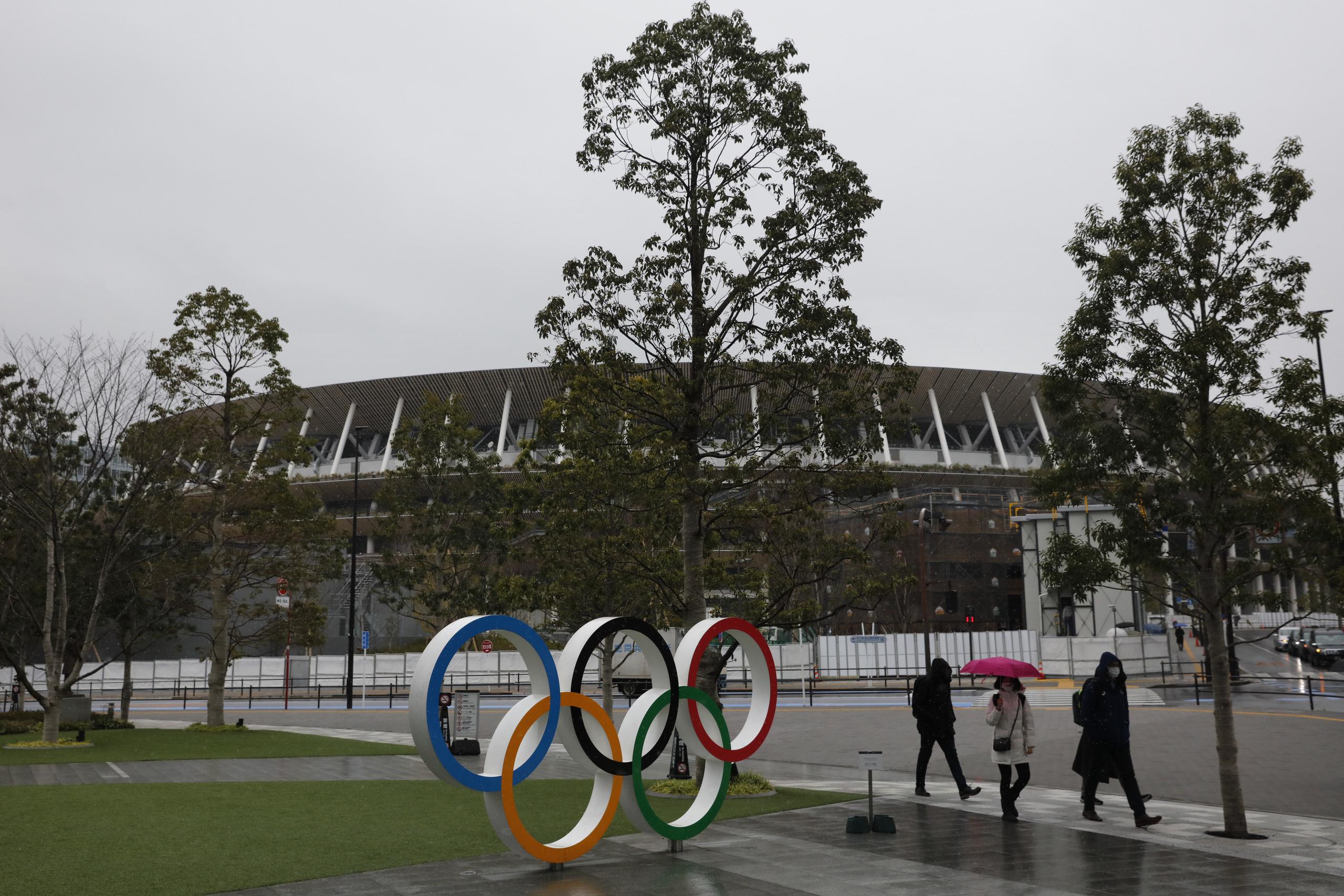 Unas personas caminan frente a los aros olímpicos cerca del estadio nacional de Tokio.