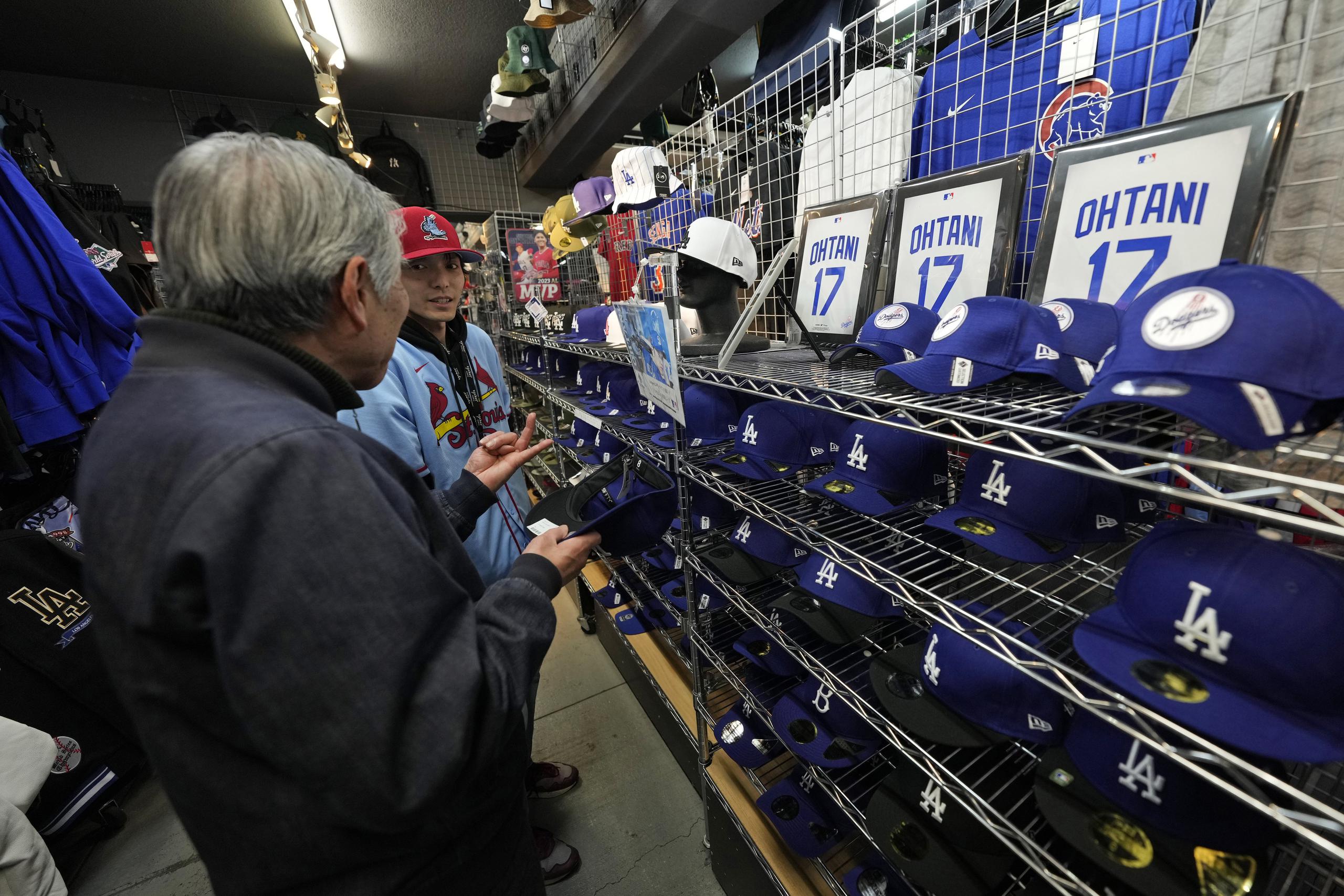Un trabajador de la tienda le ayuda a un comprador a elegir gorras de béisbol con diferentes diseños con el nombre de Shohei Ohtani en una tienda en Tokio, Japón el 29 de febrero del 2024.