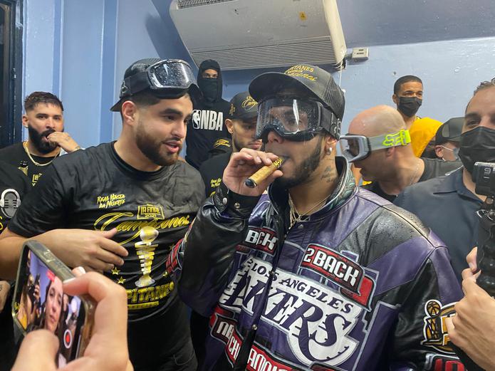 El trapero Anuel AA fuma un cigarro mientras celebra junto a su socio y manejador Frabián Eli (atrás) el campeonato del BSN ganado por los Capitanes de Arecibo.