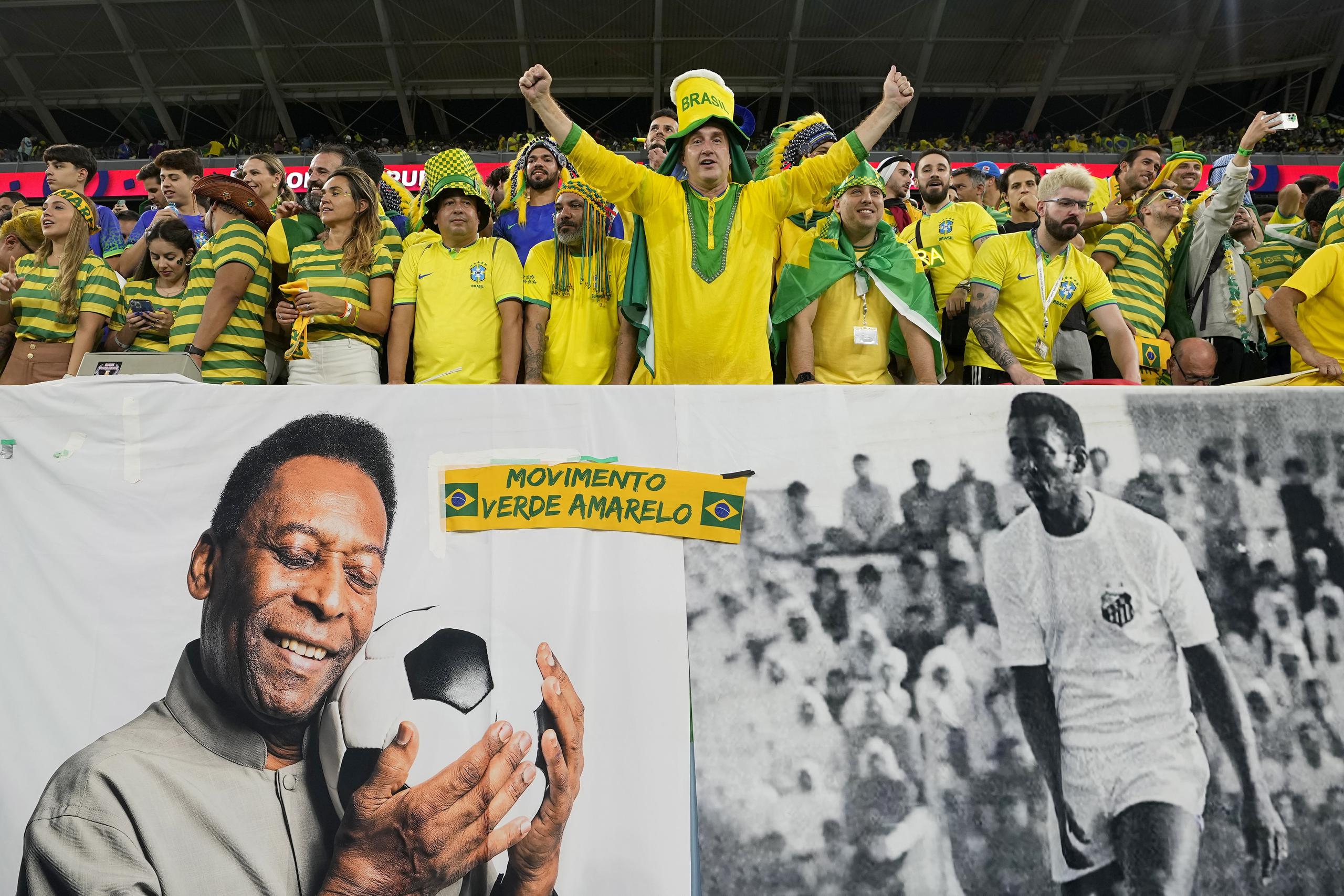 Aficionados de Brasil alientan a la selección detrás de un cartel con imágenes de Pelé.