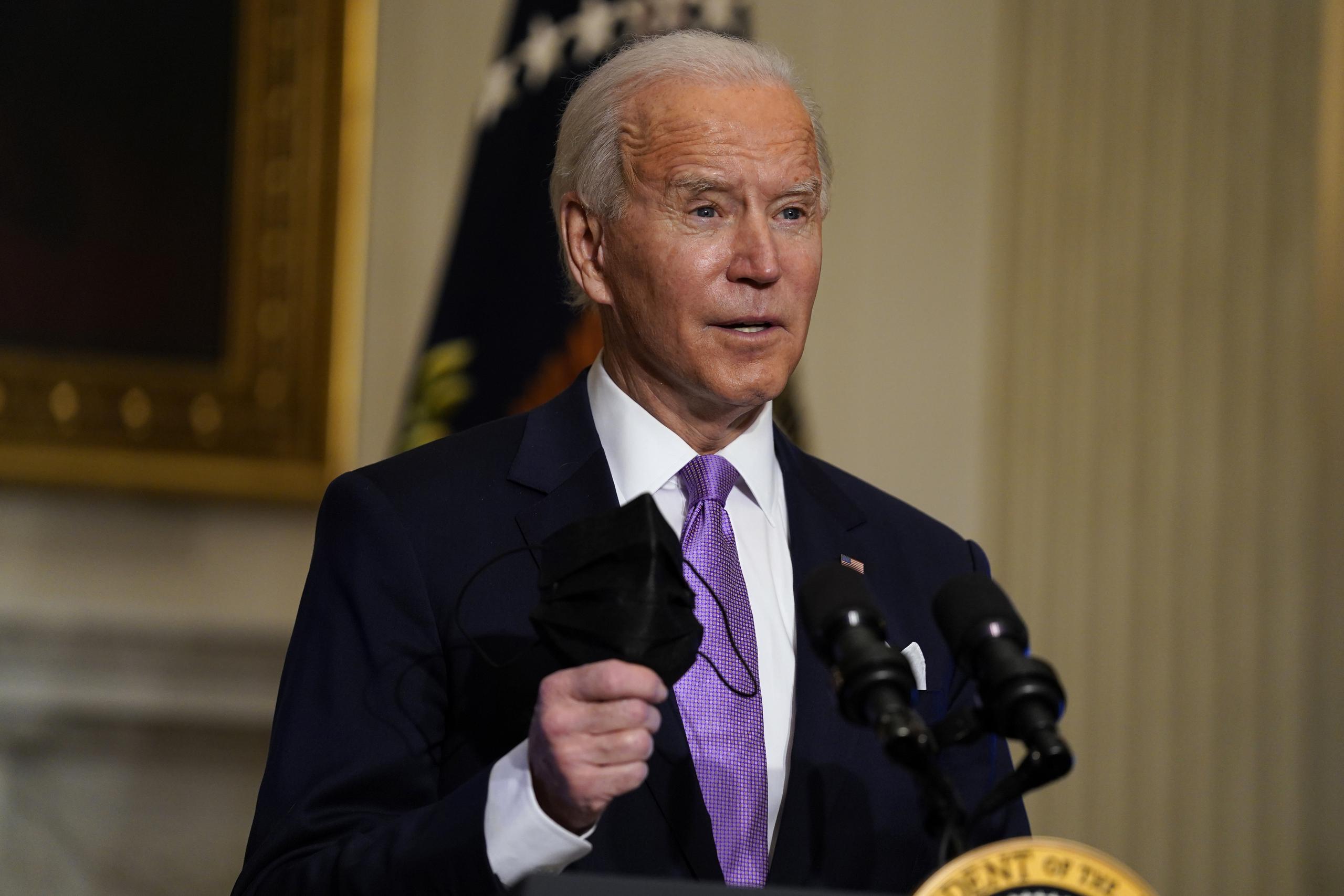 El presidente Joe Biden sostiene su mascarilla mientras hace comentarios sobre el COVID-19 en el comedor estatal de la Casa Blanca.