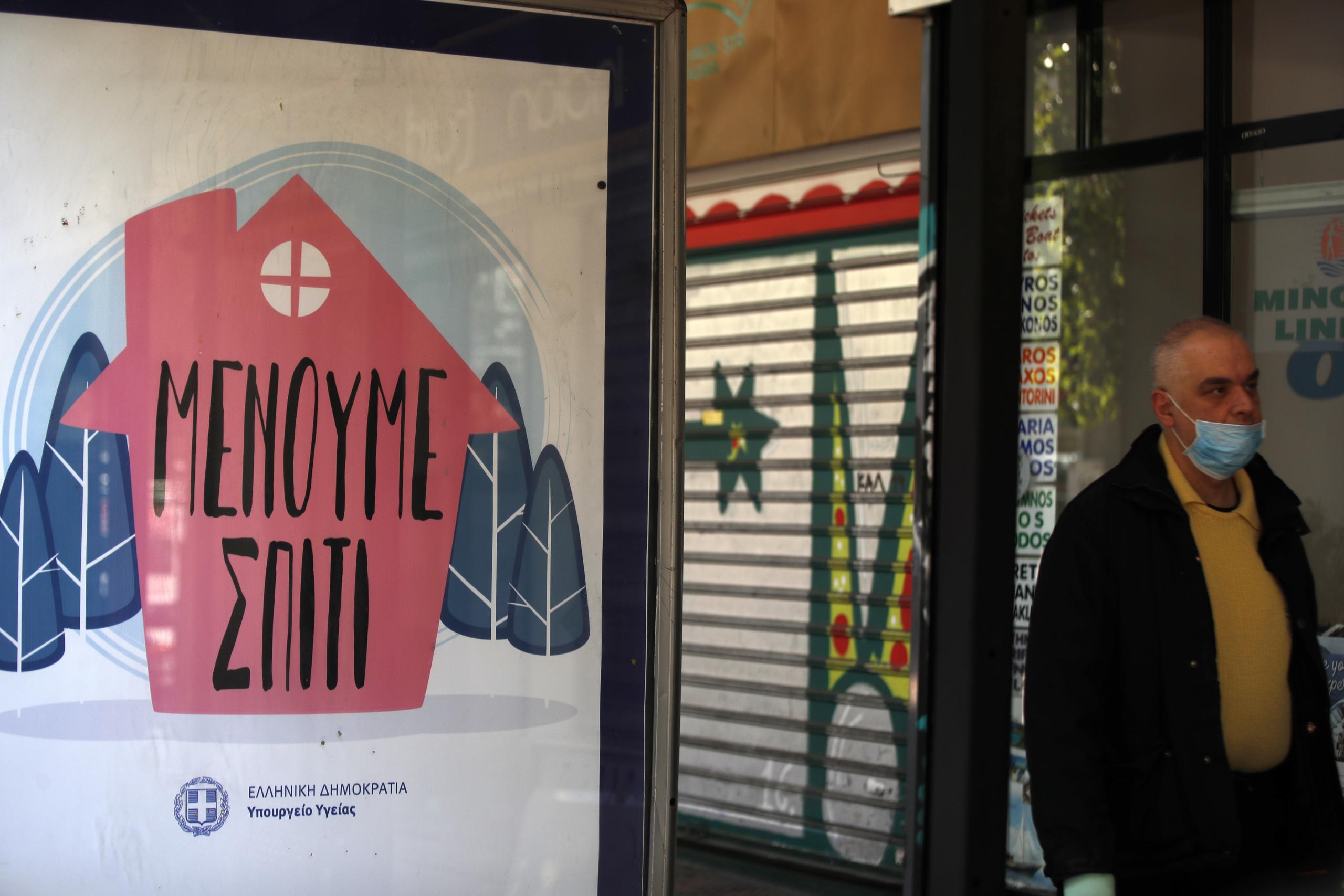 Un ciudadano con máscara camina por una calle de Grecia al lado de un letrero del gobierno con el mensaje, en griego, "quédense en casa".