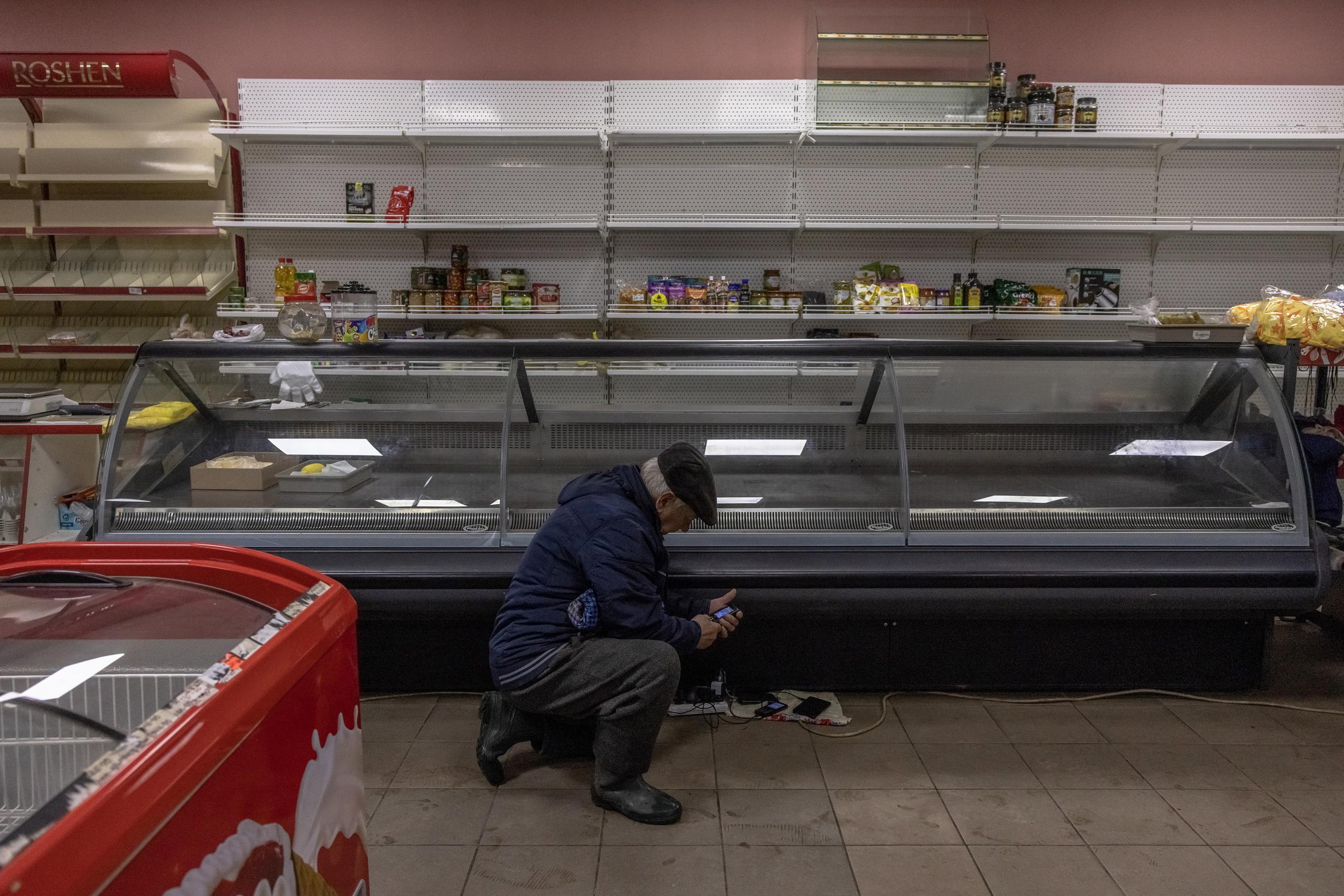 Un hombre carga su teléfono junto a un mostrador vacío dentro de un supermercado en las afueras de Jersón, al sur de Ucrania, el 26 de noviembre de 2022. EFE/EPA/ROMAN PILIPEY
