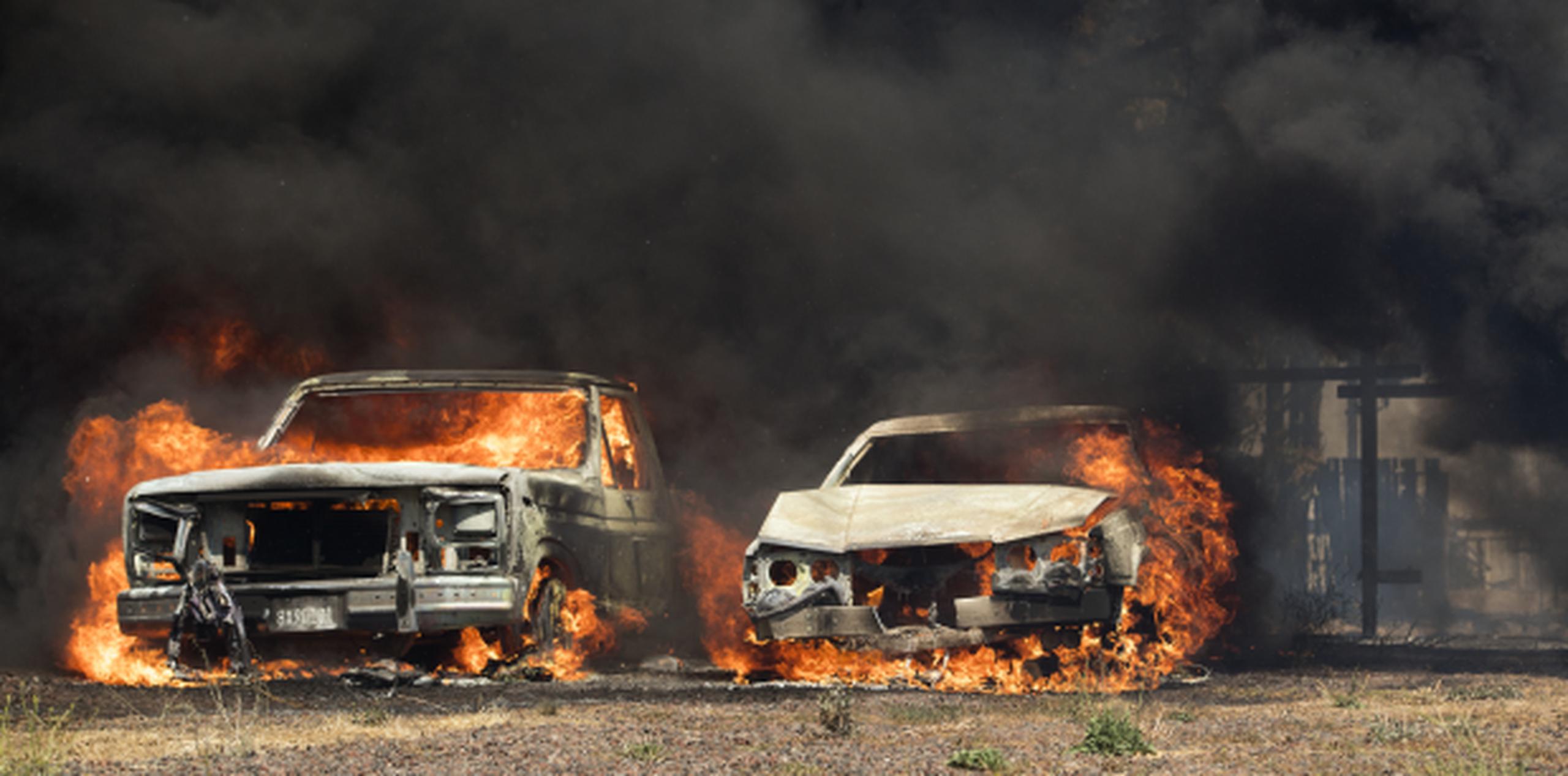 Dos vehículos arden luego de ser alcanzados por las llamas de uno de los incendios forestales que se extienden con rapidez por varias zonas de California. (AP/Josh Edelson)
