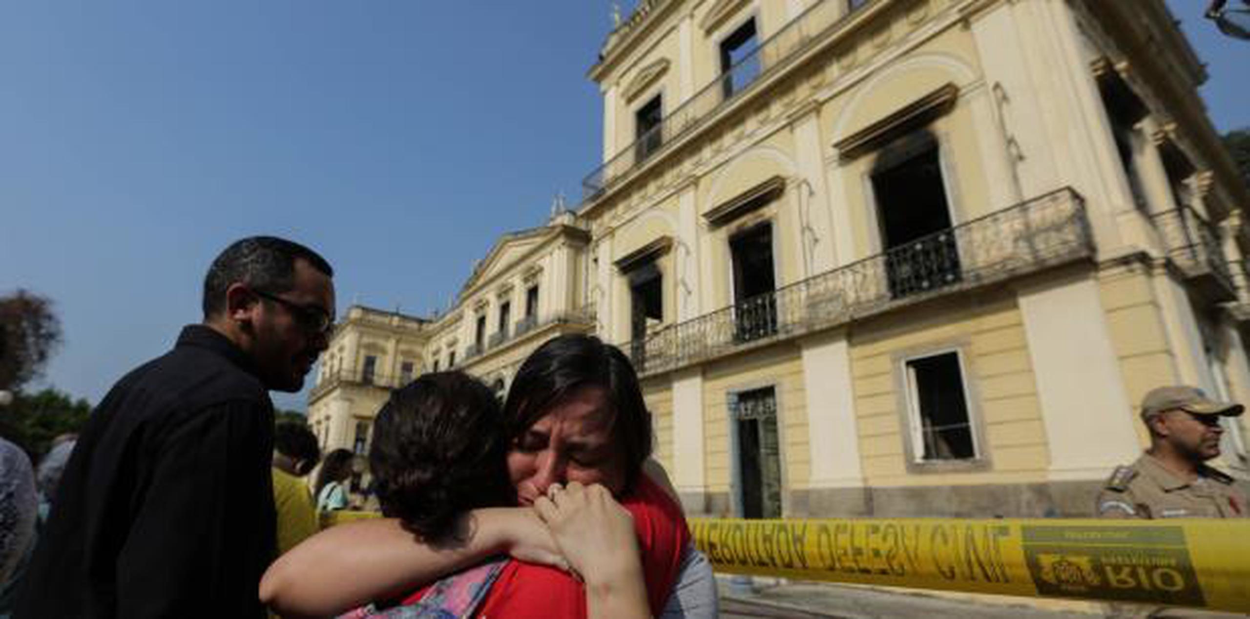 Funcionarios del Museo Nacional de Río de Janeiro lloran frente al edificio tras ser consumido por las llamas. (EFE / Antonio Lacerda)