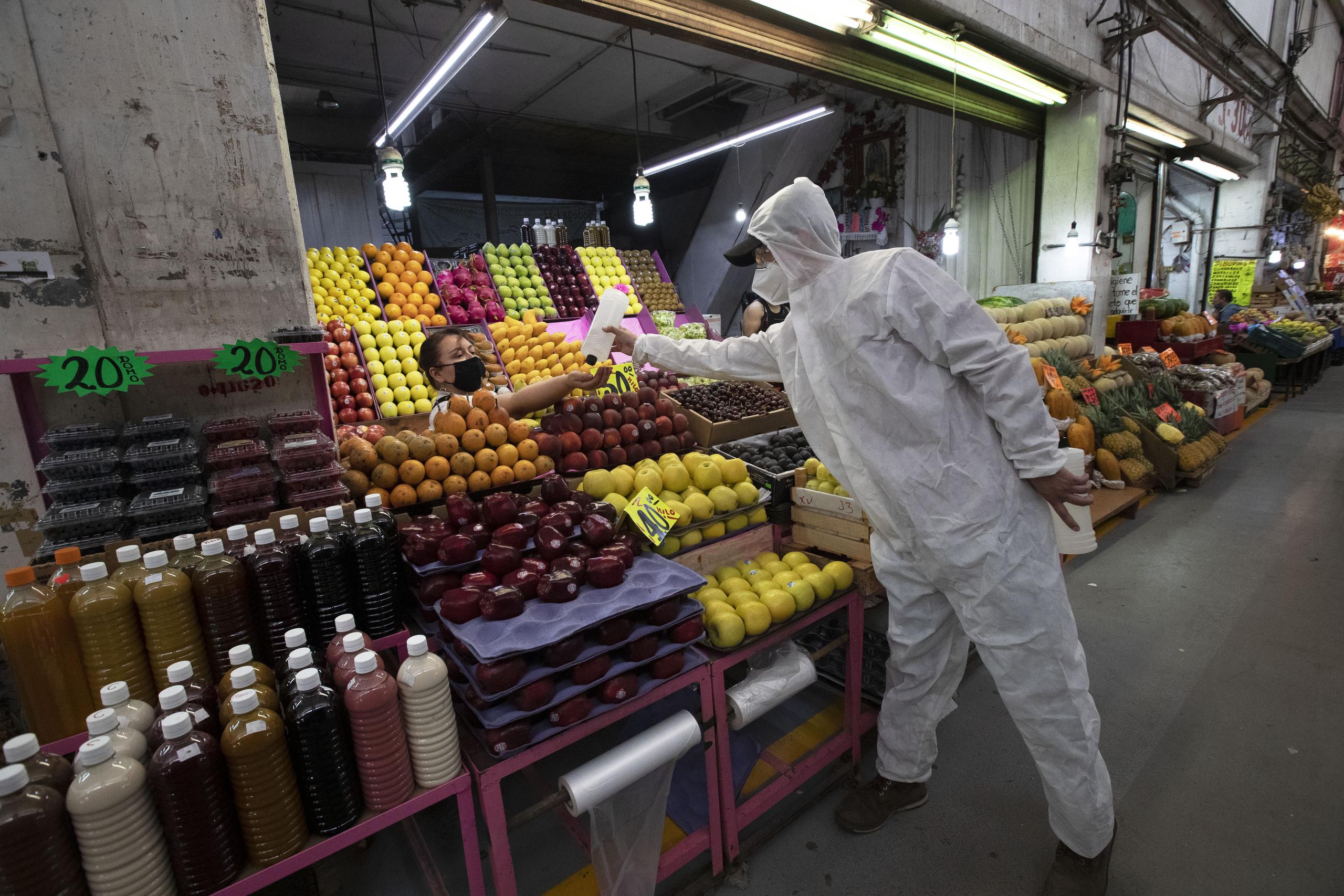 Un trabajador de salud con vestimenta para protegerse del coronavirus le da alcohol a una vendedora para que se desinfecte las manos el jueves 18 de junio de 2020 en el mercado Central de Abasto, en la Ciudad de México. (AP Foto/Marco Ugarte)