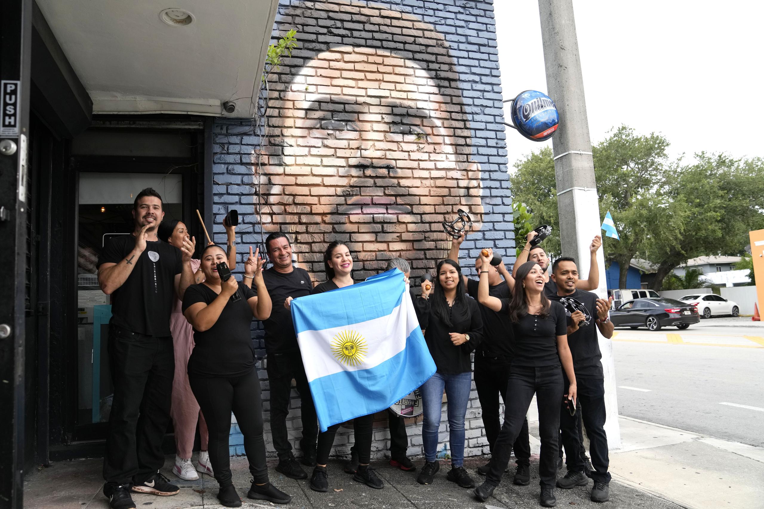 Personal del restaurante Fiorito porta una bandera de Argentina frente a un mural de Lionel Messi en Miami, el miércoles 7 de junio de 2023. (AP Foto/Lynne Sladky)