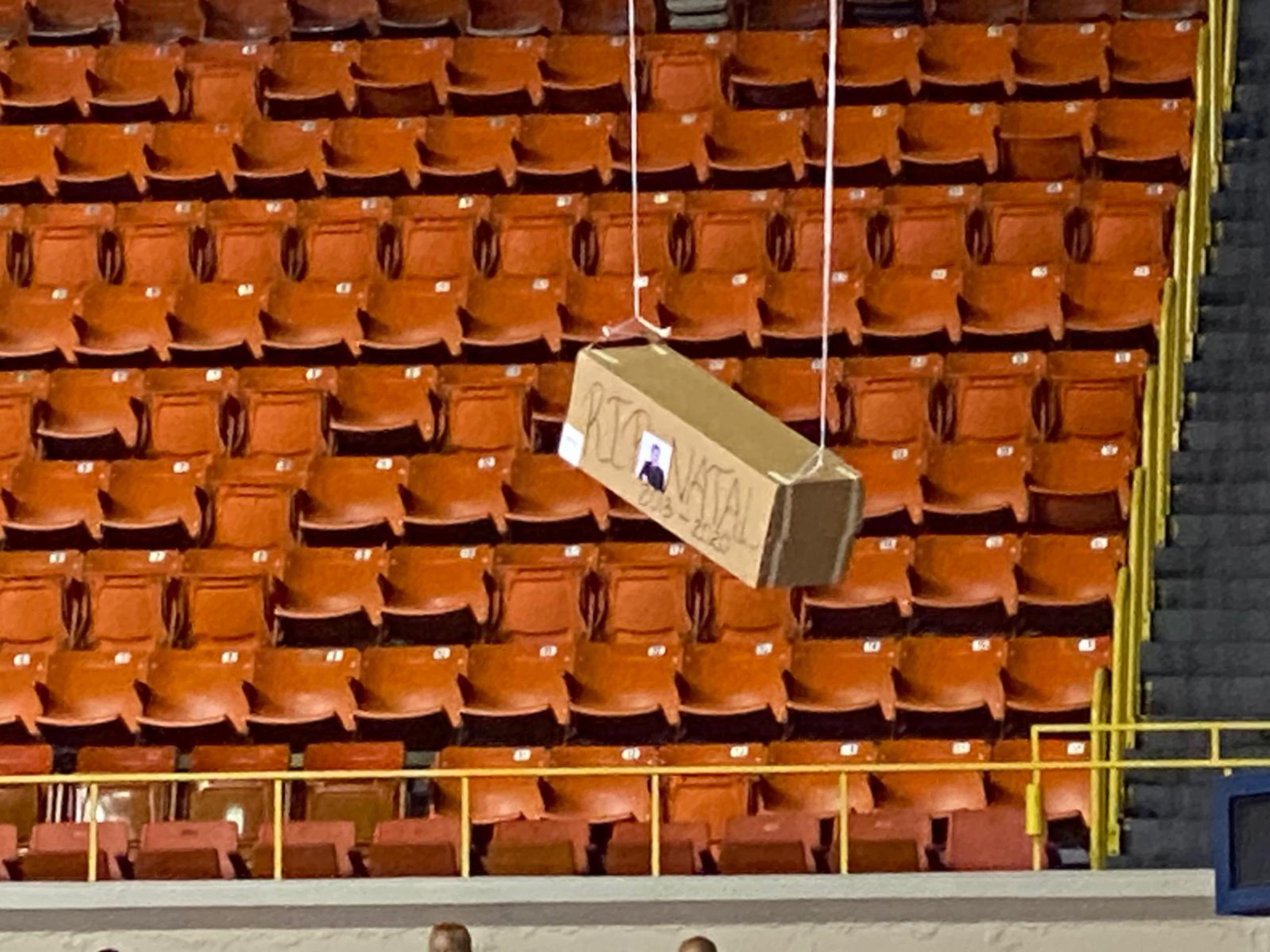La foto muestra la caja representativa de un ataud con la foto de Manuel Natal colgando del techo del coliseo Roberto Clemente. (GFR Media)