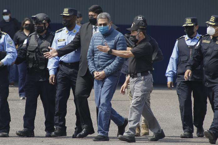 El expresidente hondureño Juan Orlando Hernández es llevado esposado a un avión que lo espera para ser extraditado a Estados Unidos desde una base de la Fuerza Aérea en Tegucigalpa, Honduras, el jueves 21 de abril de 2022. (Foto AP/Elmer Martínez)