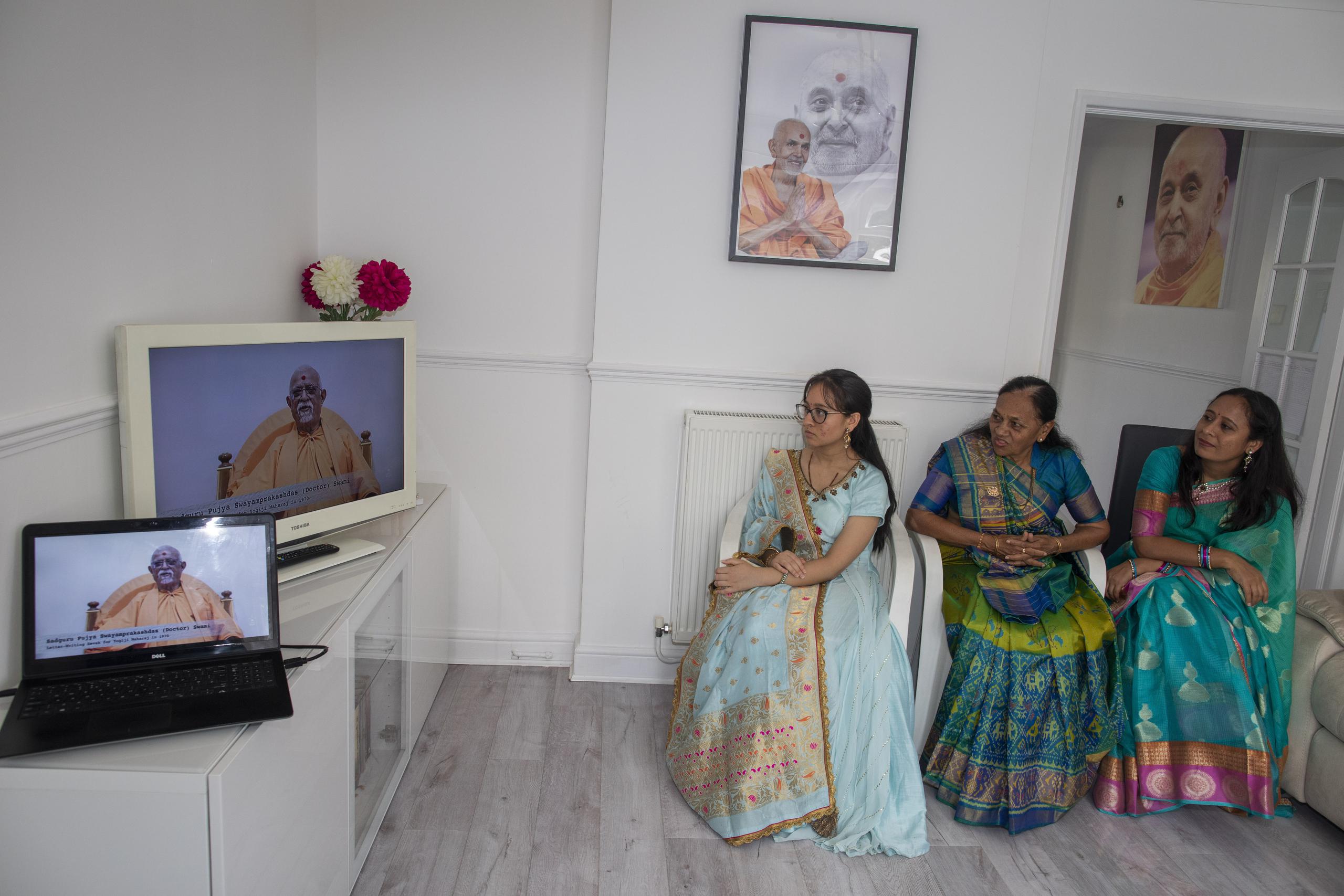 Aagna Patel, de 16 años, Pushpa Patel, de 68, y Hemali Patel, de 42, vestidas con sus mejores saris, escuchan al guru Pujya Swayamprakashdas en el televisor de su sala en Hemel Hempstead, Inglaterra