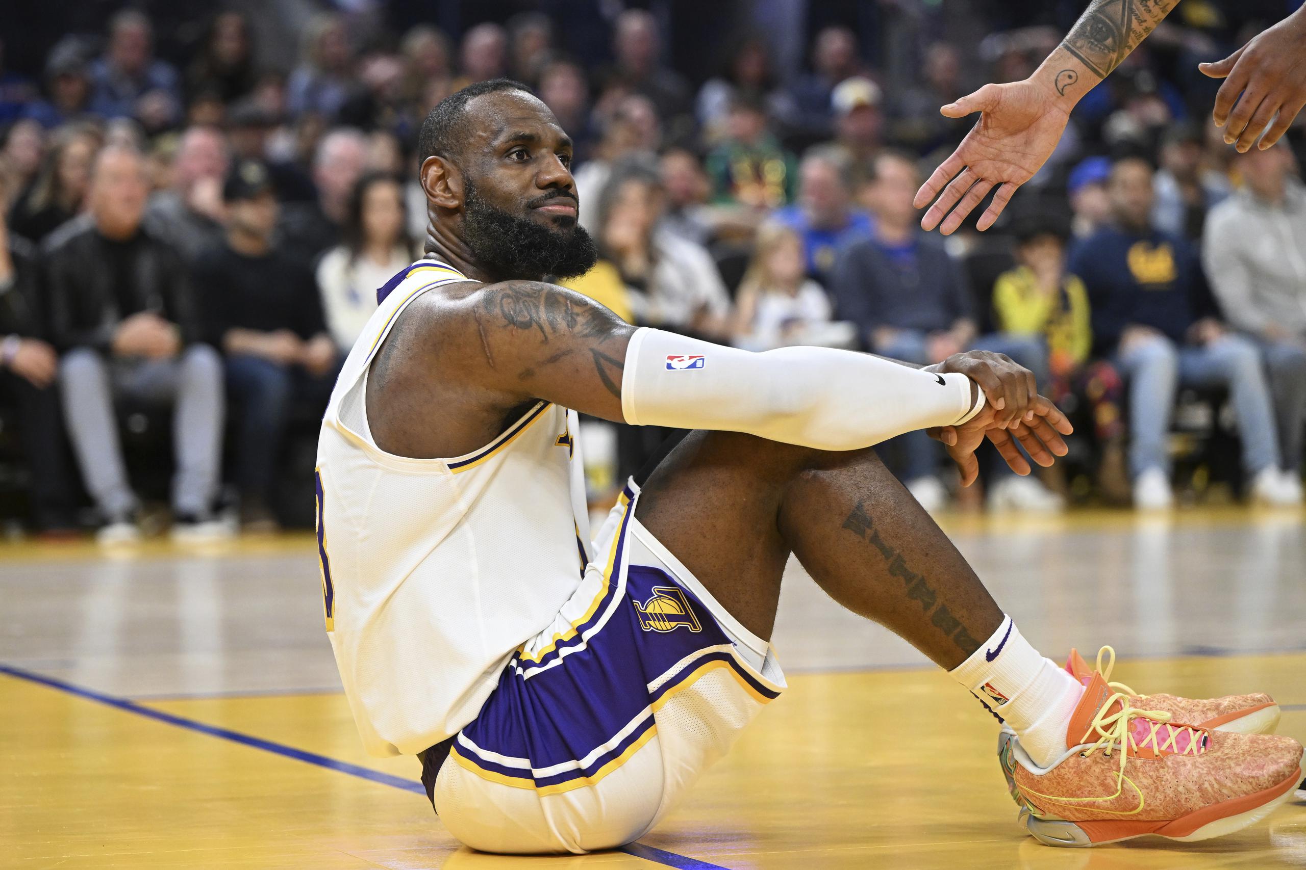 LeBron James, de los Lakers de Los Ángeles, se sienta sobre la cancha tras ser derribado durante el partido ante los Warriors de Golden State, el sábado 27 de enero de 2024 (AP Foto/Nic Coury)