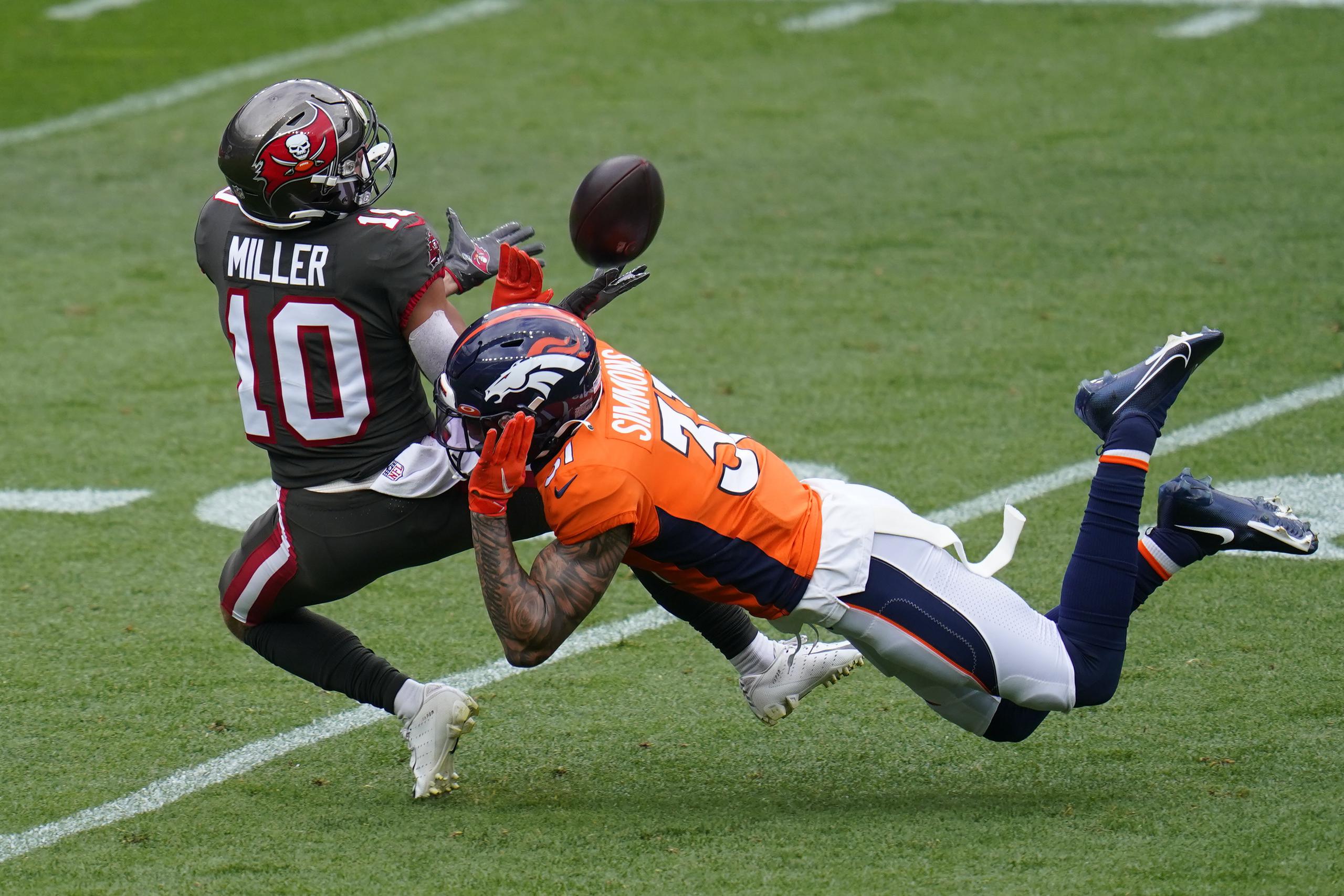 Scott Miller, 'wide receiver' de los Tampa Bay Buccaneeers, se apresta a capturar un pase mientras el 'free safety de los Denver Broncos, Justin Simmons, intenta evitarlo.