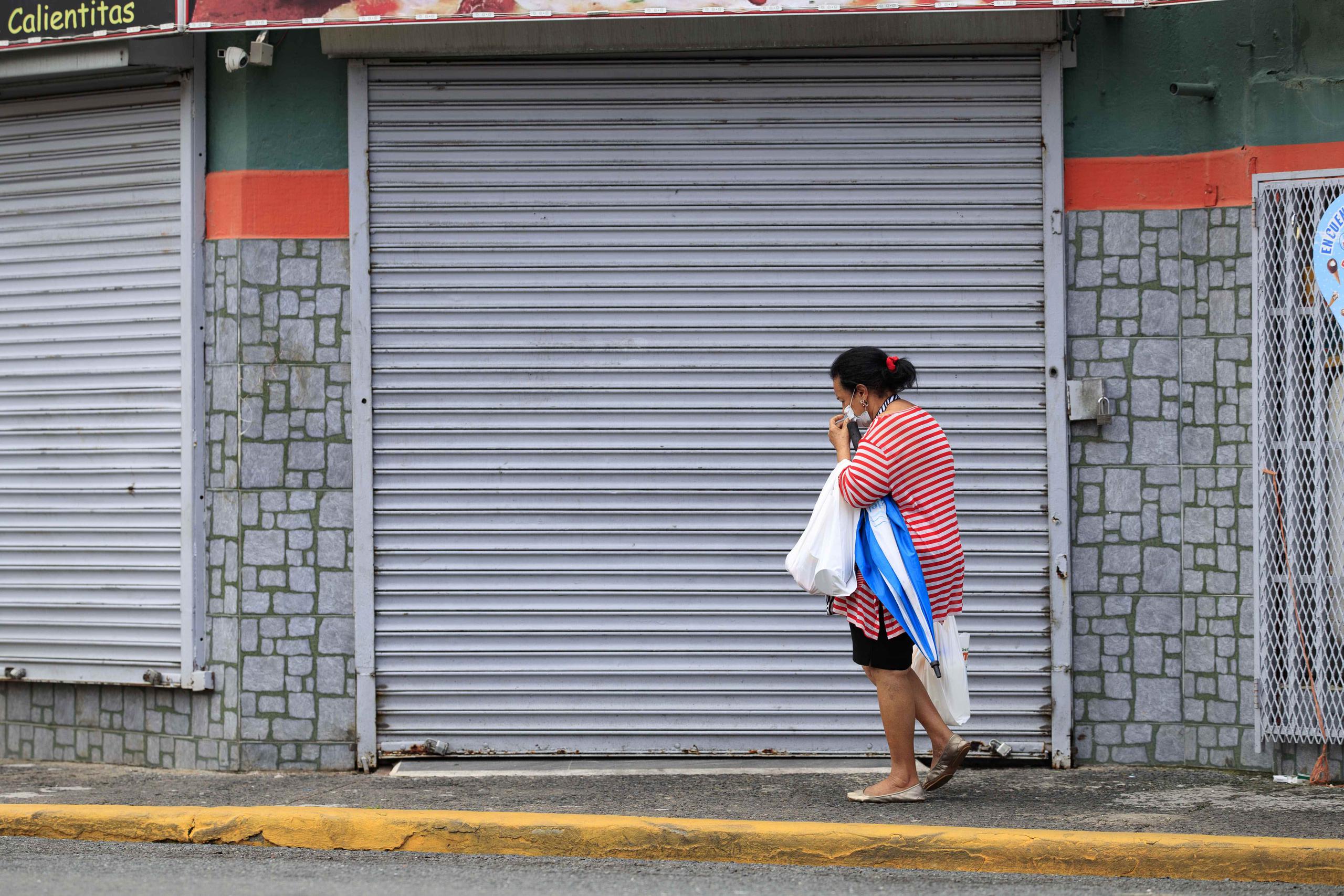El cierre forzoso de negocios y otras medidas para atajar el avance del coronavirus contribuyeron al desplome del Índice de Actividad Económica. En la foto, una mujer camina frente a un comercio cerrado en el Viejo San Juan a causa de la pandemia.