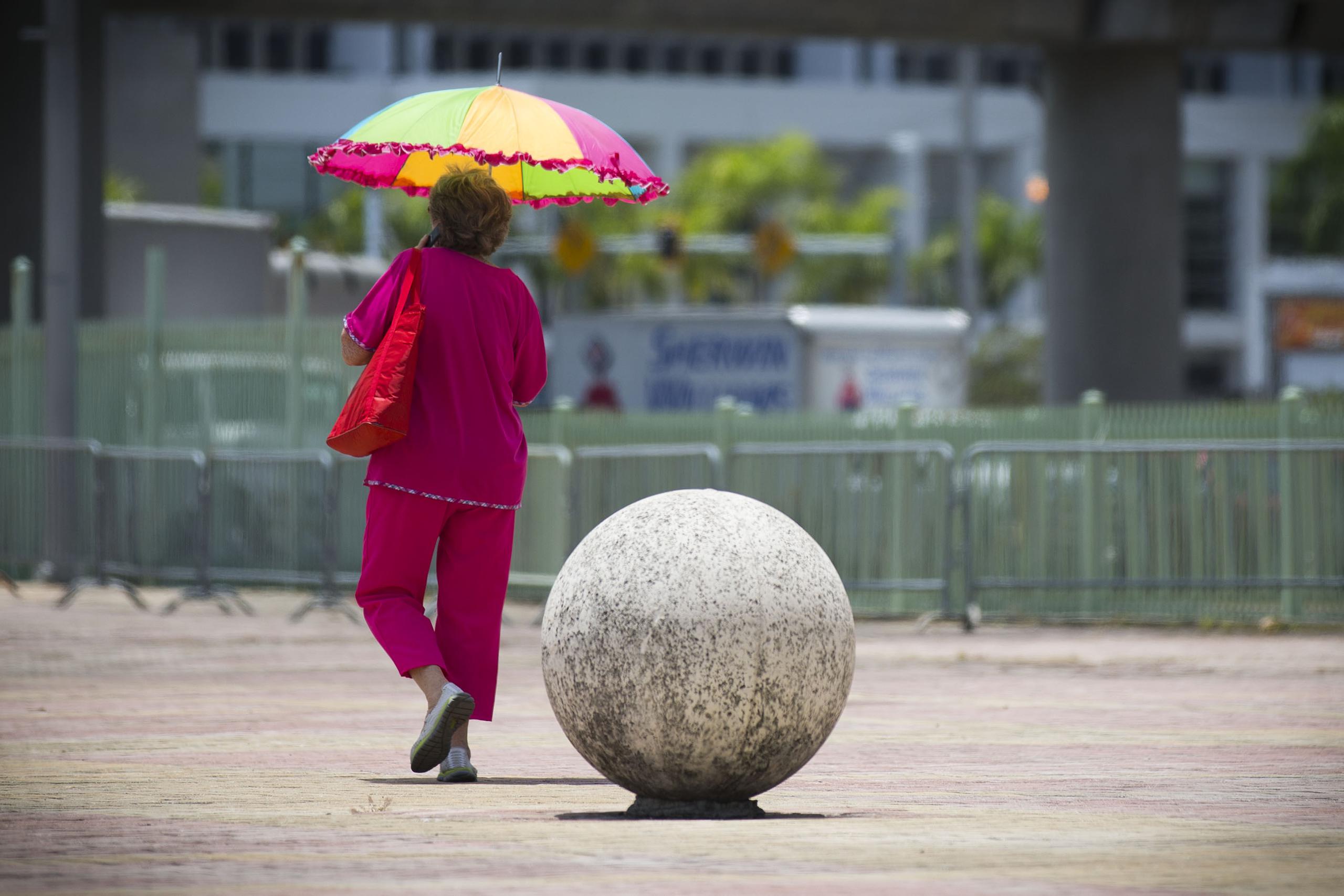 Una mujer se protege del fuerte sol de las doce del medio dia con su tambien colorida sombrilla mientras caminaba por un area de la plaza frente al Coliseo de Puerto Rico ( Choliseo ) en direccion al Tren Urbano .