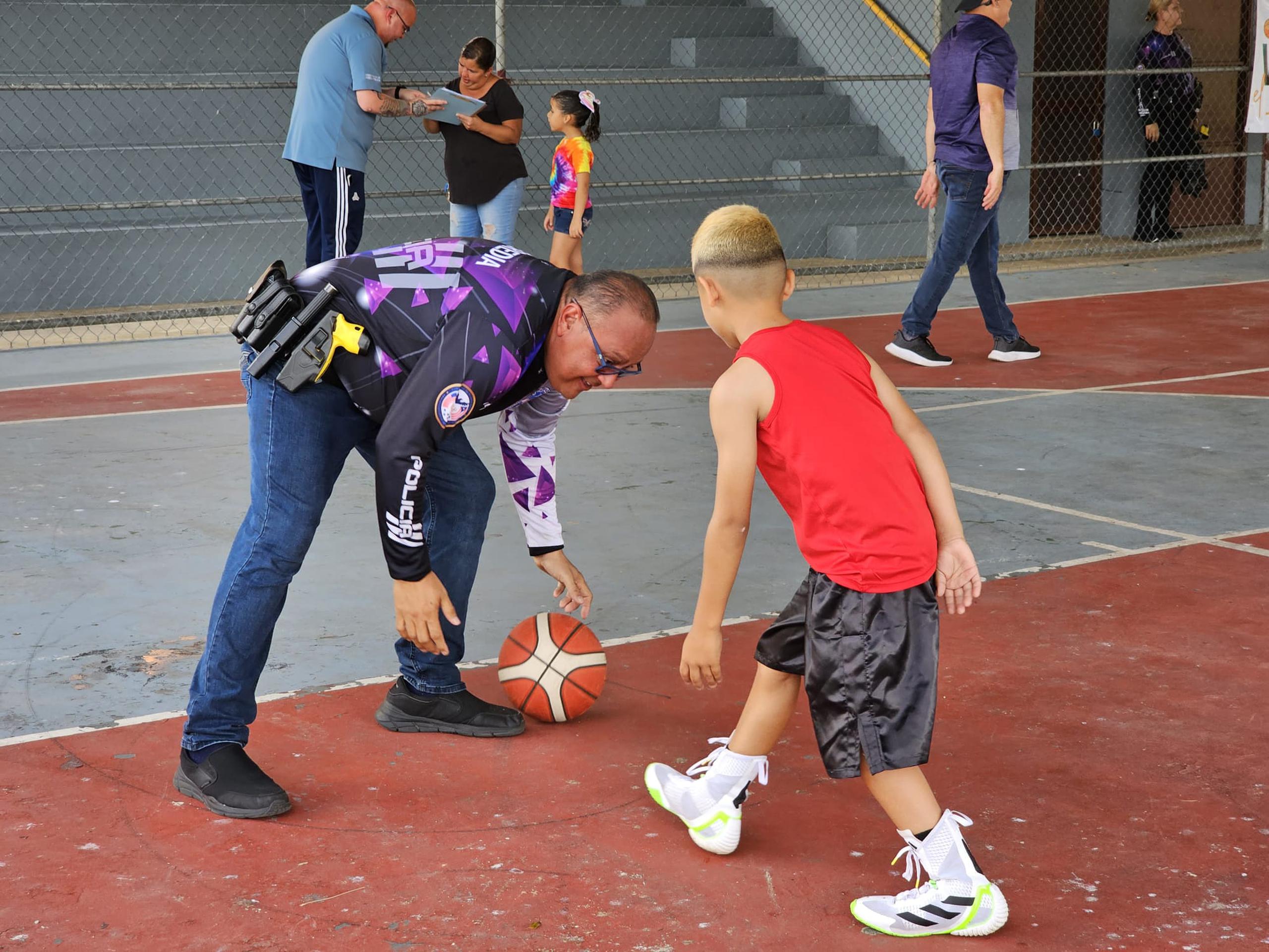 Una niño juega baloncesto con un agente de la Policía como parte del impacto comunitario que realizan en el residencial Pedro Zorrilla de Manatí.