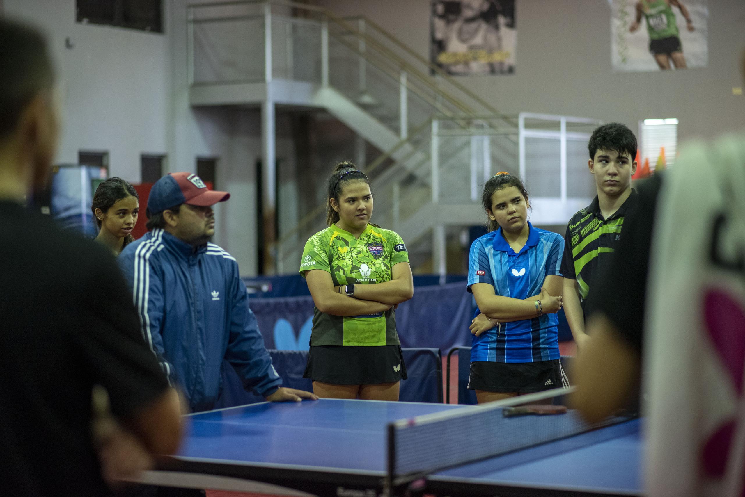 Bladimir Díaz, entrenador del equipo nacional femenino, y un grupo de atletas escuchan mientras otra persona les ofrece una instrucción.