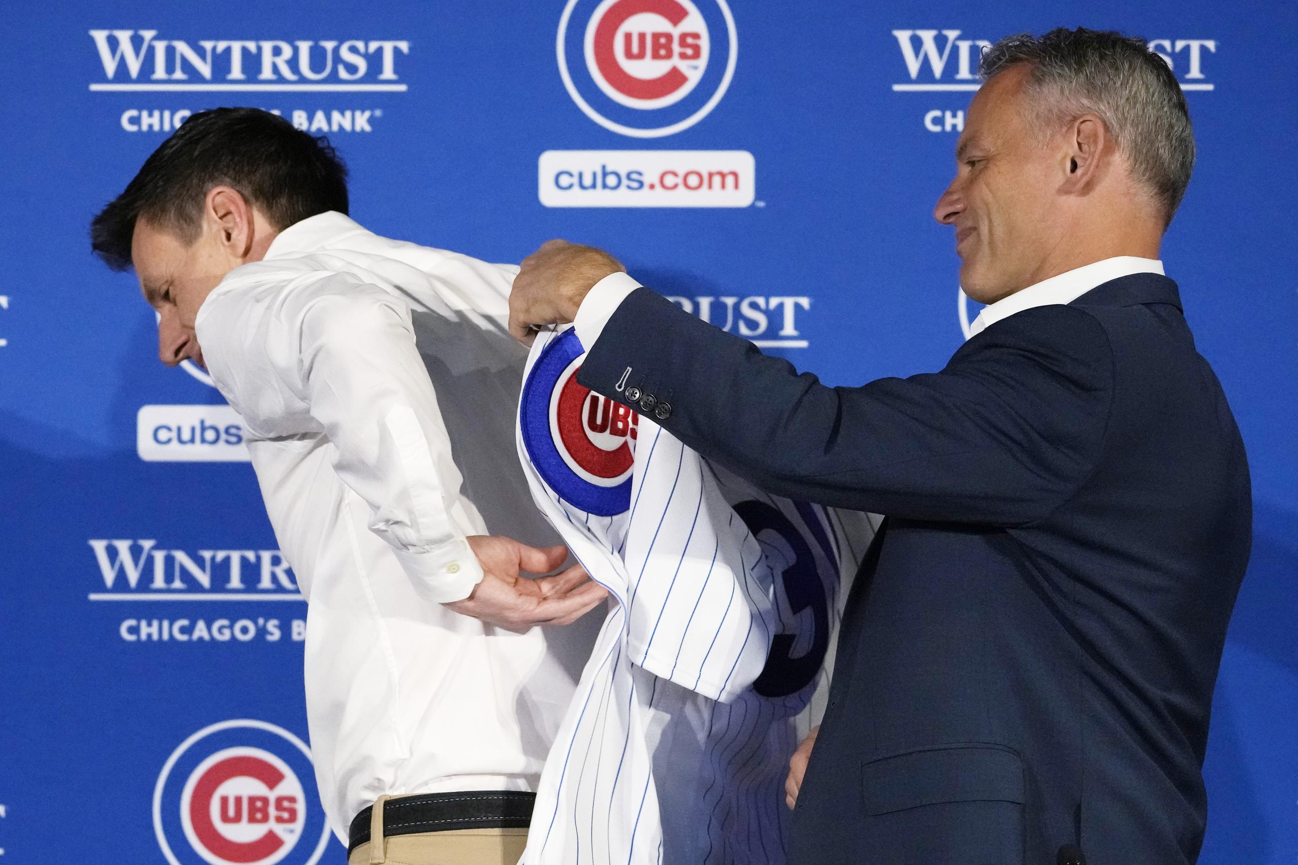 Jed Hoyer, presidente de los Cubs, asiste a su nuevo dirigente Craig Counsell a ponerse la camisa de los Cubs.