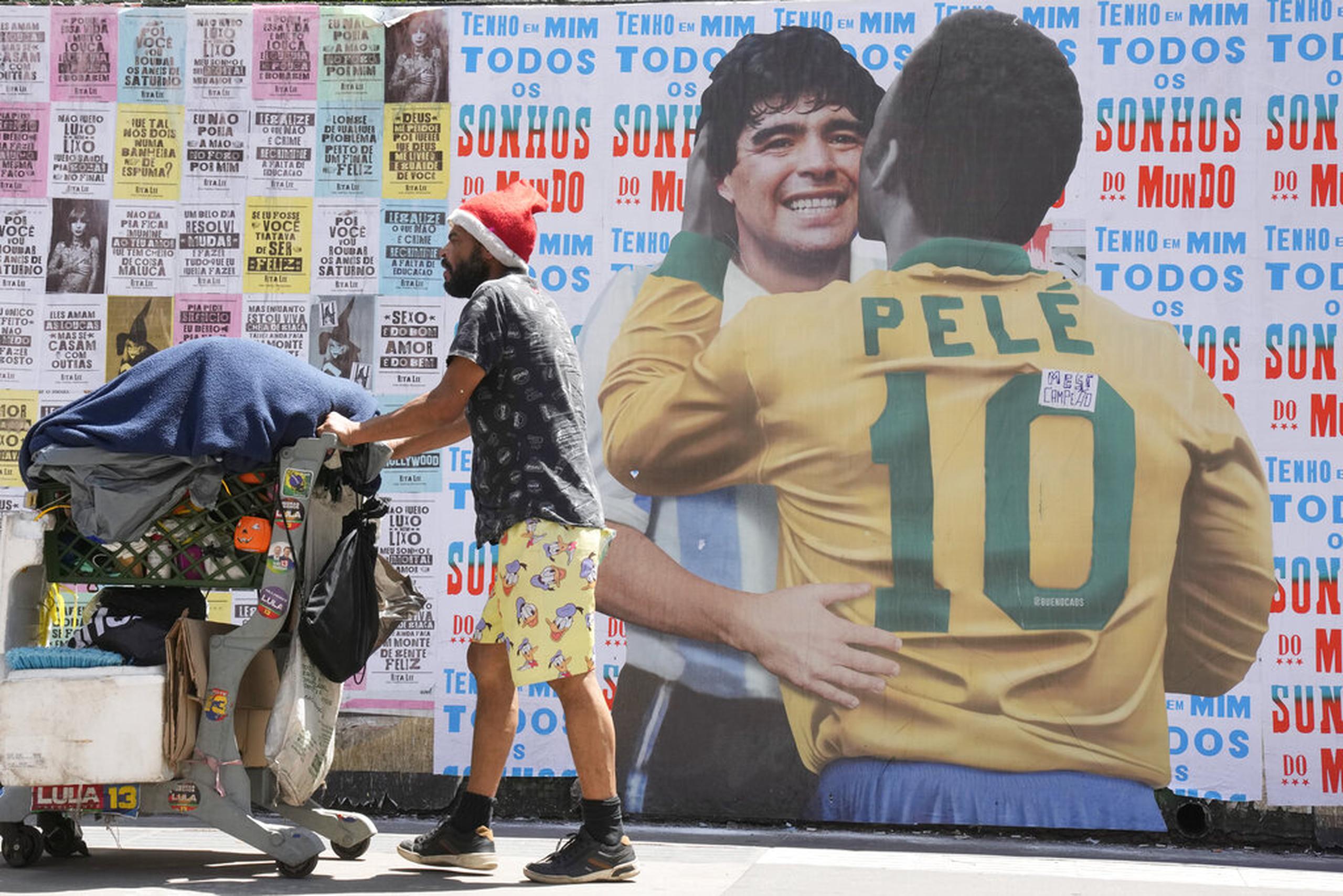 Un hombre empuja un carrito lleno de basura para reciclar frente a un mural en el que se muestra al astro brasileño Pelé abrazando a la difunta estrella del fútbol, el argentino Diego Maradona, en Sao Paulo, Brasil.