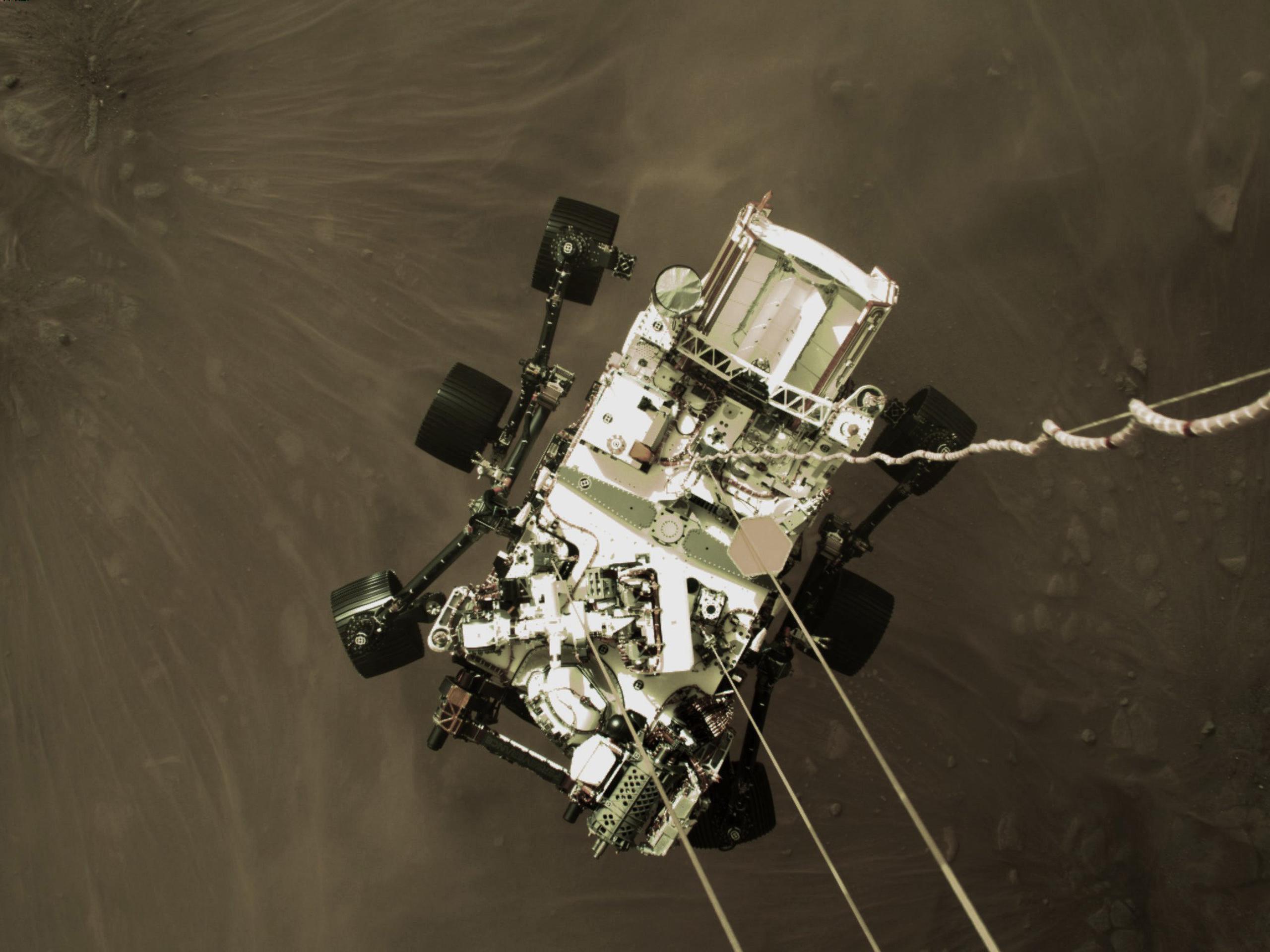 Imagen provista por NASA del Perseverance mientras desciende por cables a la superficie de Marte.
