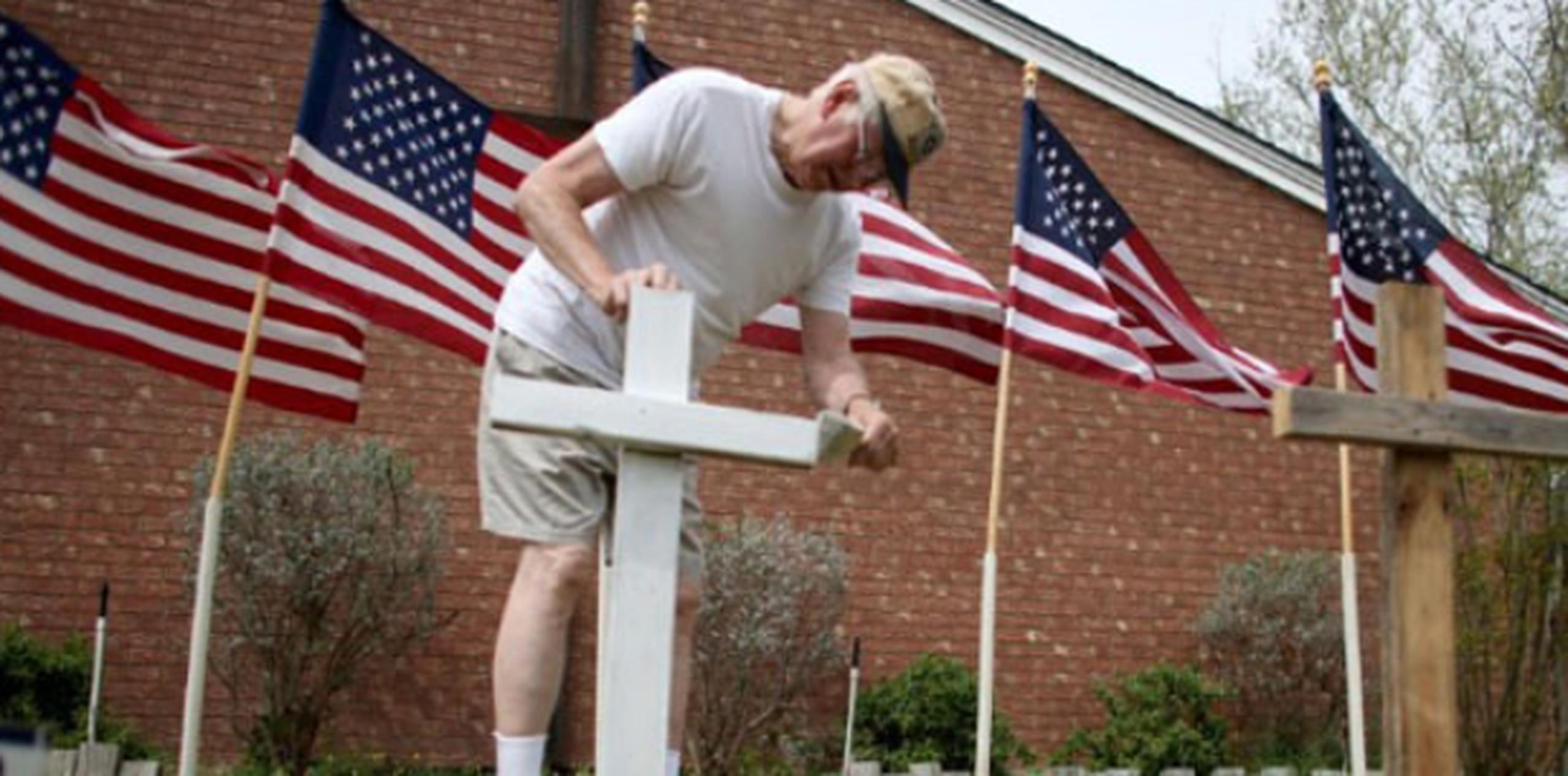 Bob Gordon pinta cruz, colocada al frente de 16 banderas de Estados Unidos, en recuerdo a las víctimas de la matanza ocurrida ayer en Fort Hood, Texas.(AFP)