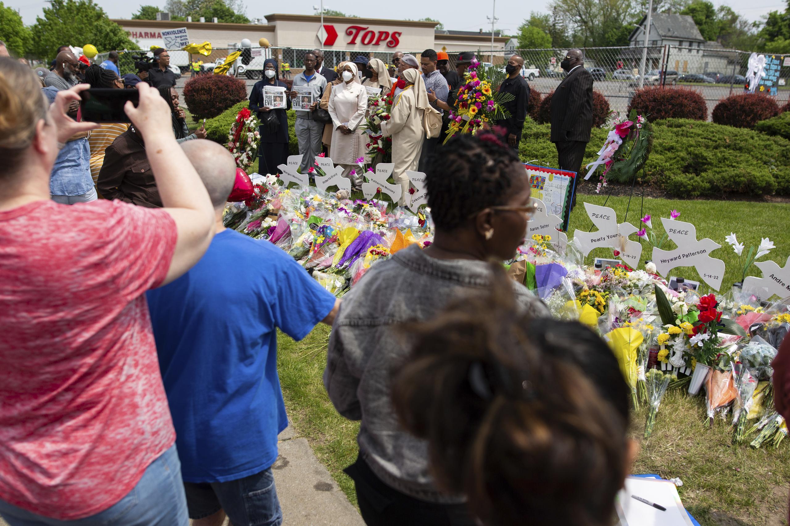 La gente se reúne en torno a un monumento para las víctimas del tiroteo en el supermercado de Buffalo fuera del Tops Friendly Market el sábado 21 de mayo de 2022, en Buffalo, Nueva York.