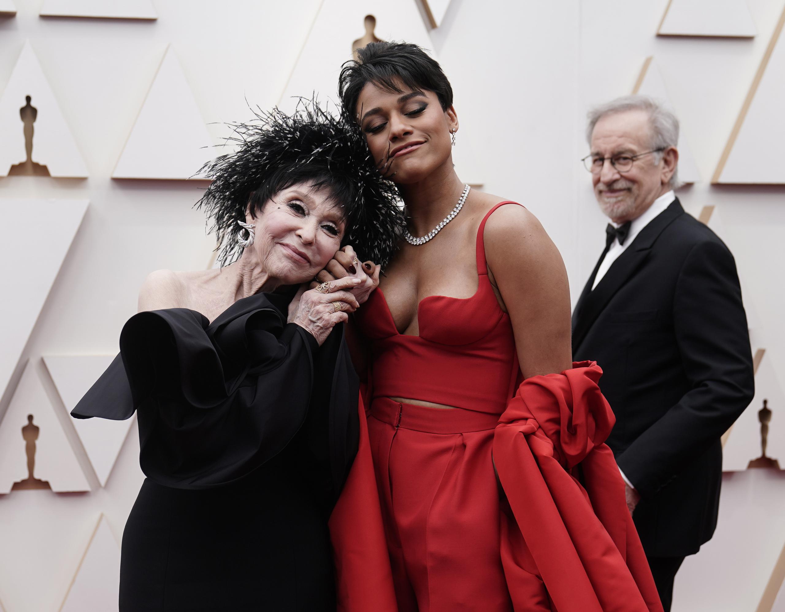 Rita Moreno, izquierda, y Ariana DeBose llegan a los Oscar el 27 de marzo de 2022 en el Teatro Dolby en Los Angeles. Al fondo mira Steven Spielberg. (Foto AP/Jae C. Hong)