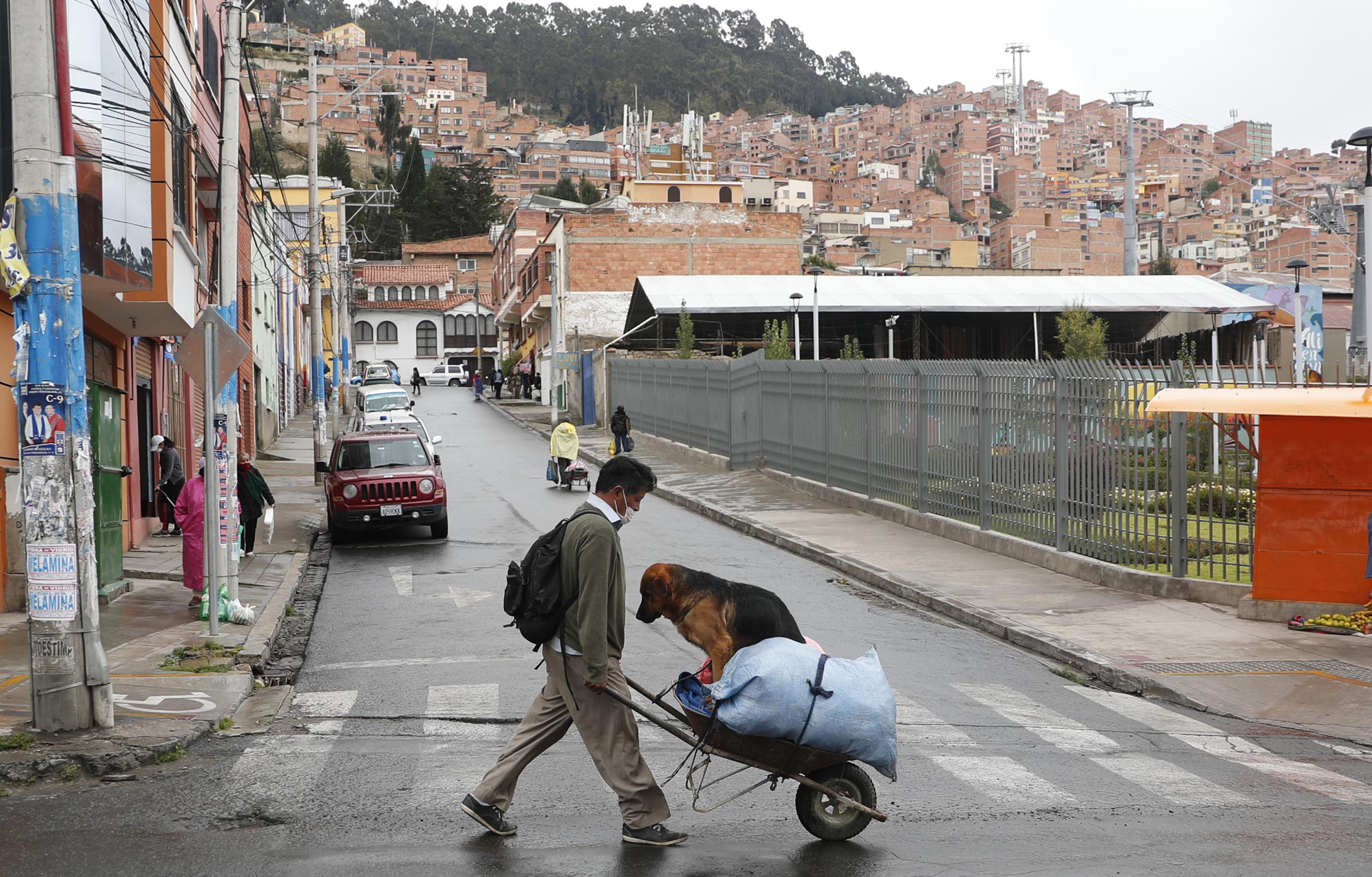 En esta imagen, tomada el 17 de abril de 2020, un hombre empuja una carreta cargada con sacos y con su perro durante la estricta cuarentena contra el coronavirus que permite que los residentes realicen compras de primera necesidad en las mañanas, en La Paz, Bolivia.