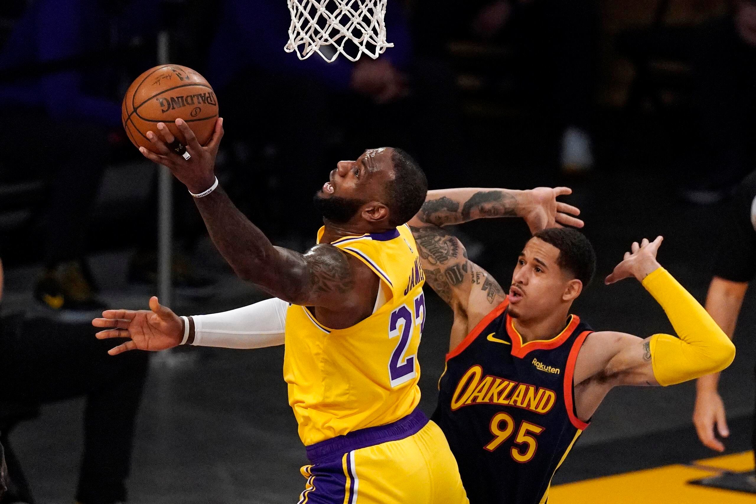 LeBron James, de los Lakers, realiza un incómodo tiro frente a Juan Toscano-Anderson, de los Warriors, en un partido "play-in" de la NBA jugado este año. La fase deja a los equipos clasificados entre los puesto siete al 10 en suspenso de clasificación a la postemporada hasta que juguen el minitorneo.