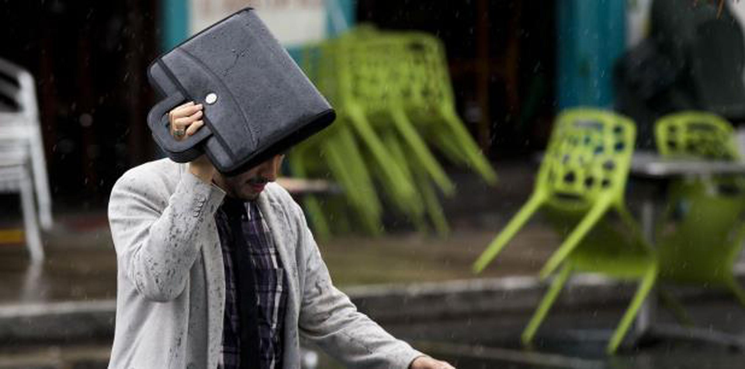 Un hombre utiliza su cartapacio para cubrirse de la lluvia. (Archivo)