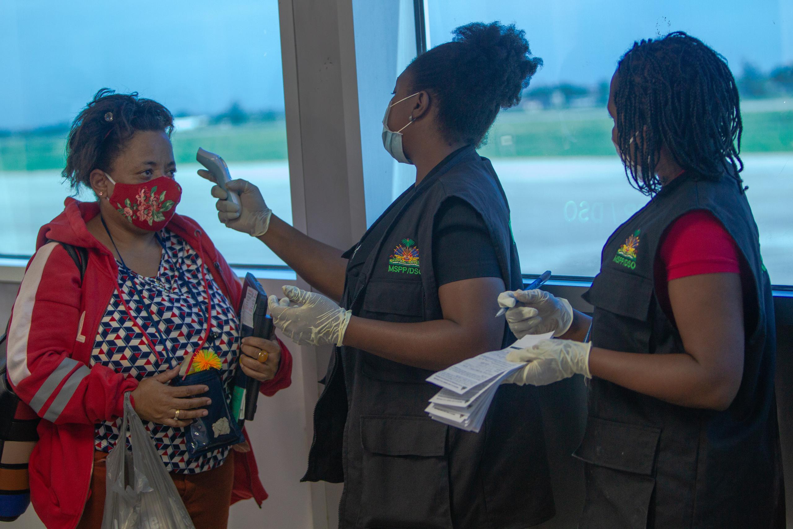 Trabajadores del aeropuerto toman la temperatura y el registro a los pasajeros que llegan al Aeropuerto Internacional Toussaint Louverture de Puerto Príncipe (Haití).