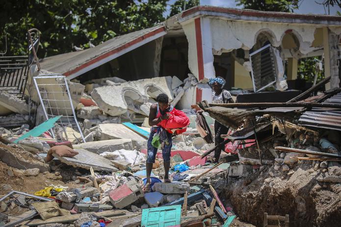 Unas mujeres recuperan sus pertenencias de sus casas destrozadas el domingo 15 de agosto de 2021, en Les Cayes, Haití, luego de un sismo de magnitud 7,2. (AP Foto/Joseph Odelyn)