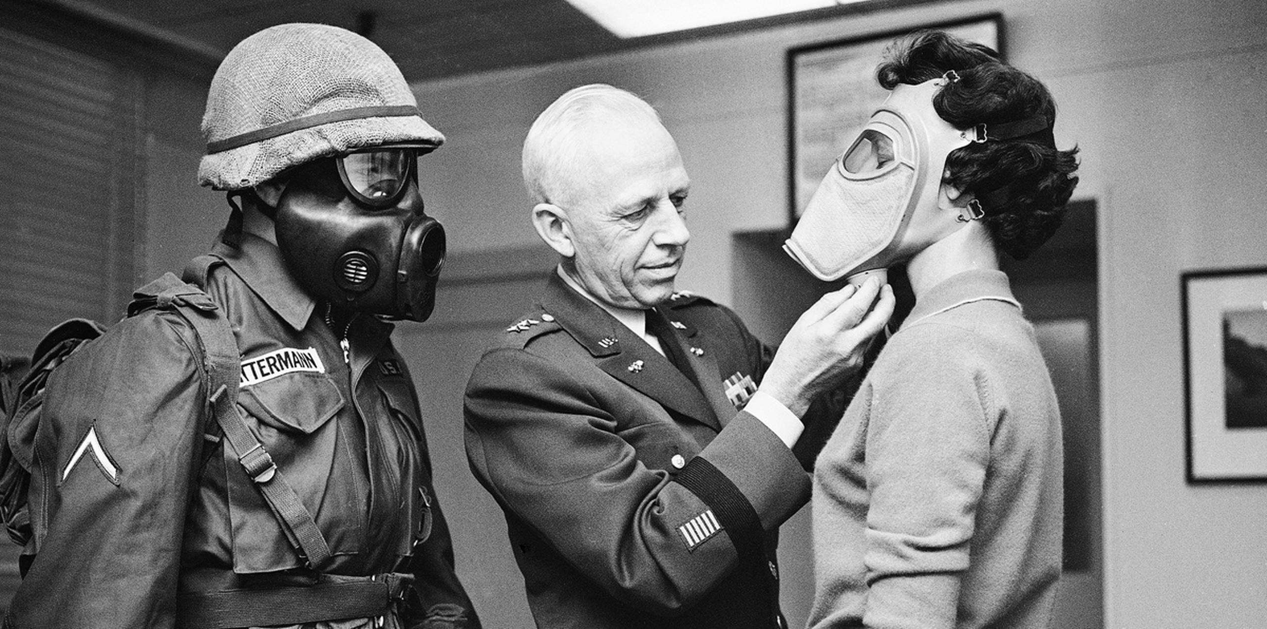 En esta imagen de archivo, tomada el 19 de enero de 1959, el soldado Warner Bitterman (izquierda) observa mientras el jefe de armas químicas del ejército, el mayor general Marshall Stubbs (centro), hace pruebas con una nueva máscara antigás con la secretaria Margaret Francis en su oficina en el Pentágono, Washington. (AP)