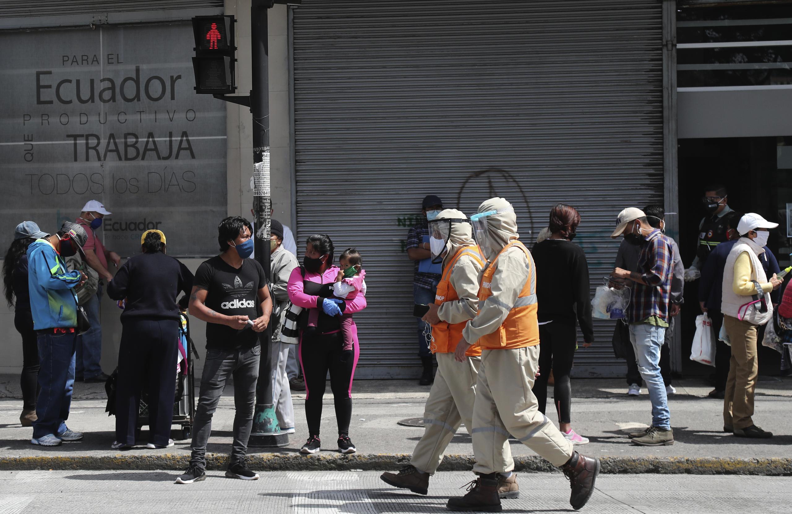 Trabajadores con trajes de protección para prevenir el nuevo coronavirus caminan junto a peatones en Quito, Ecuador