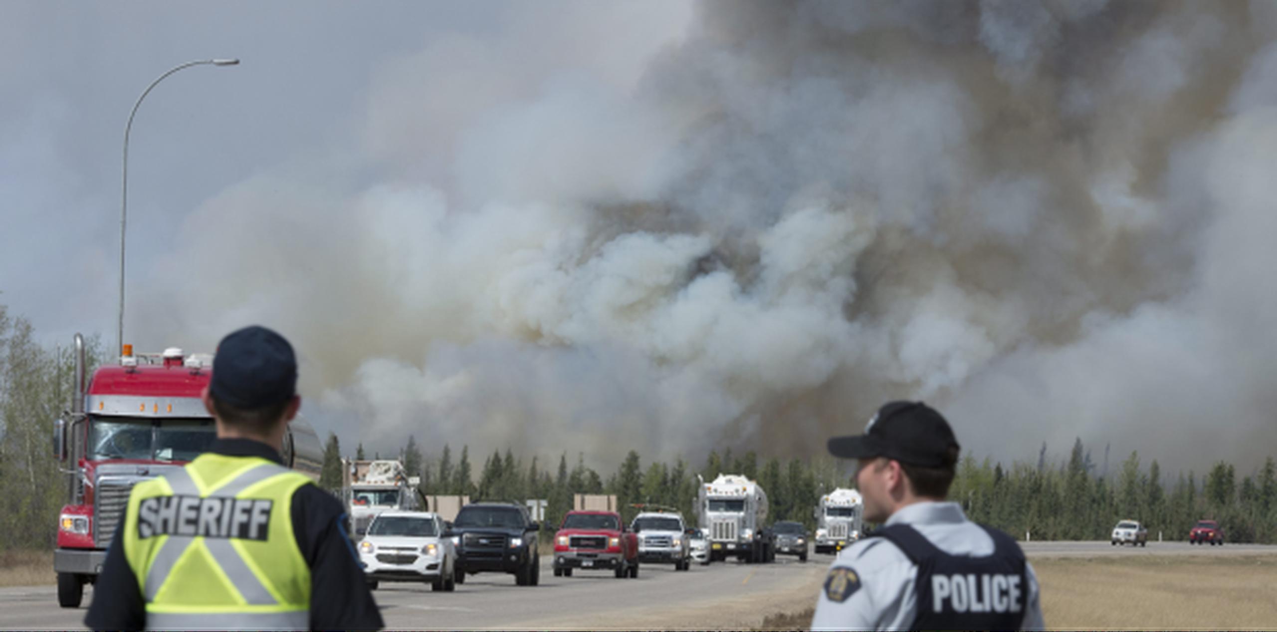 La policía de Canadá vigila uno de los convoyes de camiones y vehículos mientras continúa la evacuación masiva de personas en toda el área afectada por el enorme incendio forestal que ya amenaza con extenderse a otra provincia. (Jonathan Hayward /The Canadian Press via AP)