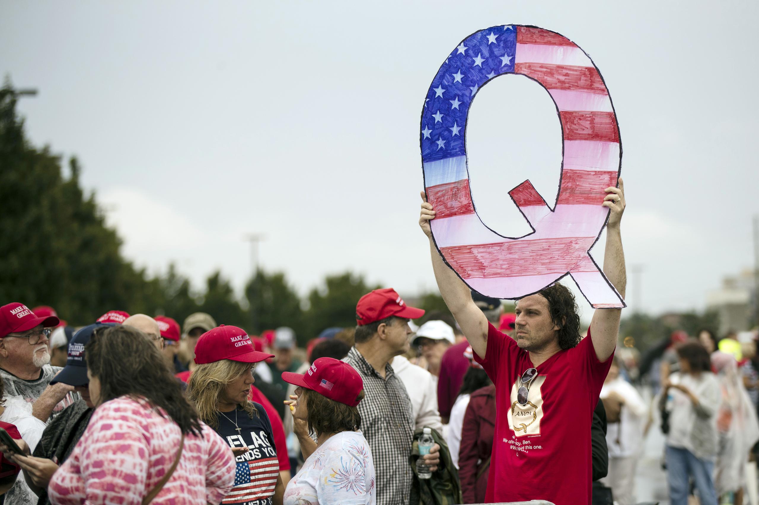 Una persona sostiene en lo alto una Q mientras espera con otras para asistir a un acto de campaña del presidente Donald Trump en Wilkes-Barre, Pensilvania