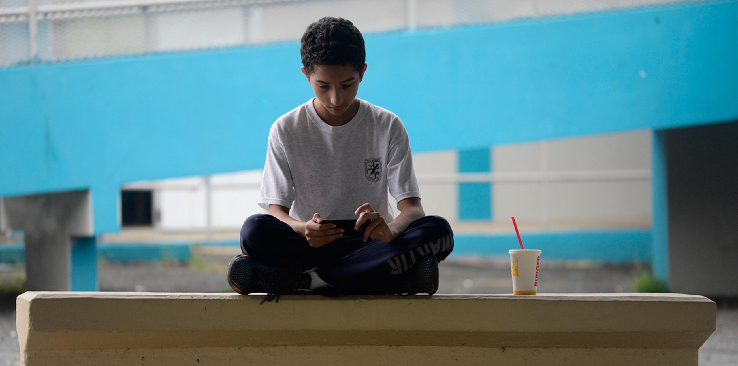 Un niño juega con un celular sentado en el patio de la escuela primaria Ramón Marín Solá, en Guaynabo, que abrió sus puertas como centro comunitario tras el paso del huracán. (AP)