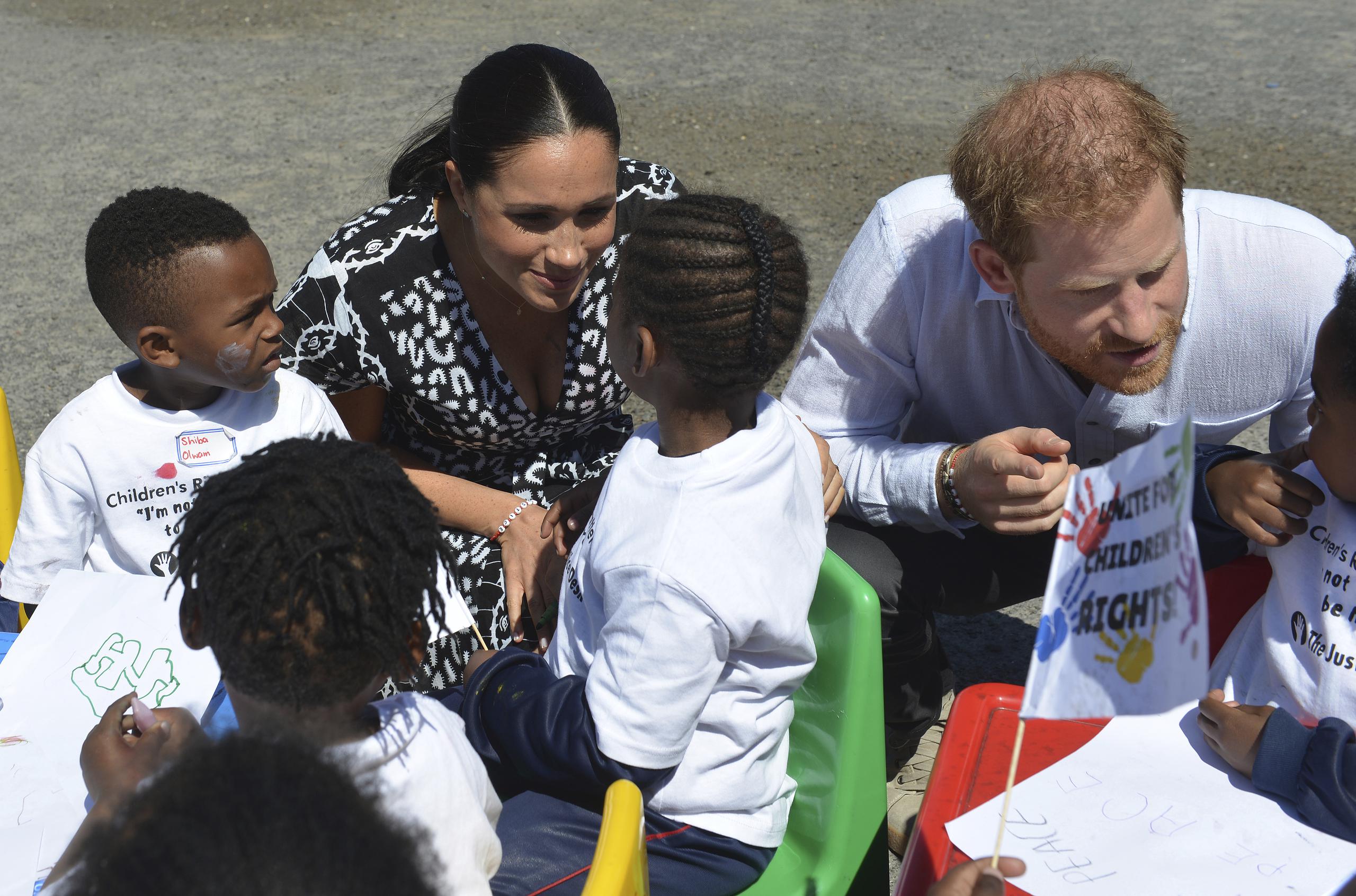 El príncipe Enrique y su esposa Meghan Markle conversan con niños durante una visita a una iglesia de Ciudad del Cabo, Sudáfrica.