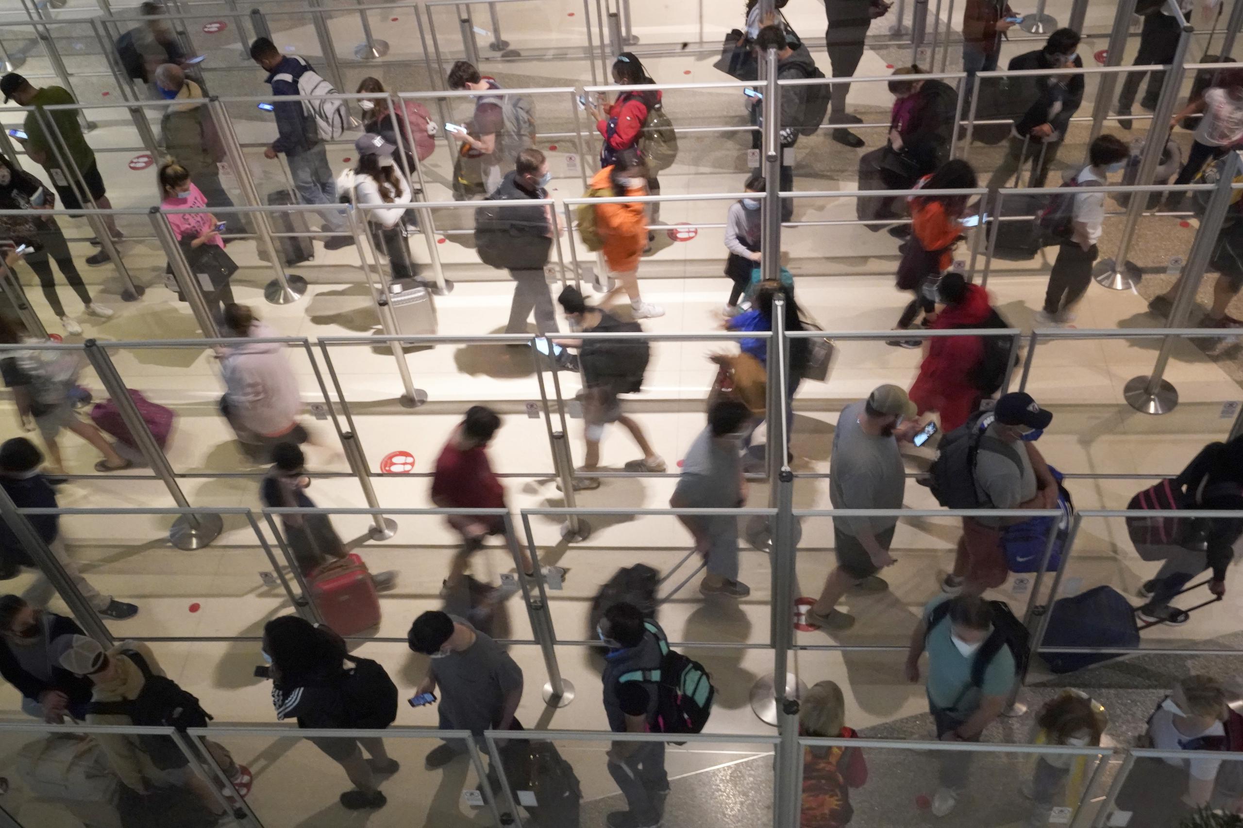 Viajeros con mascarillas como medida de prevención contra el contagio de coronavirus hacen fila para una revisión de seguridad en el aeropuerto Love Field, en Dallas, el viernes 31 de diciembre de 2021.